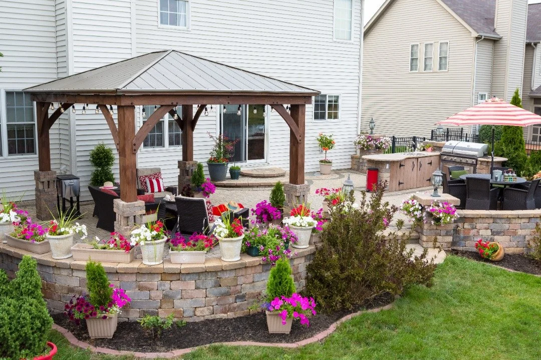 Charming backyard outdoor living space with a wooden bench, vibrant flowers, potted plants, and cozy patio seating.
