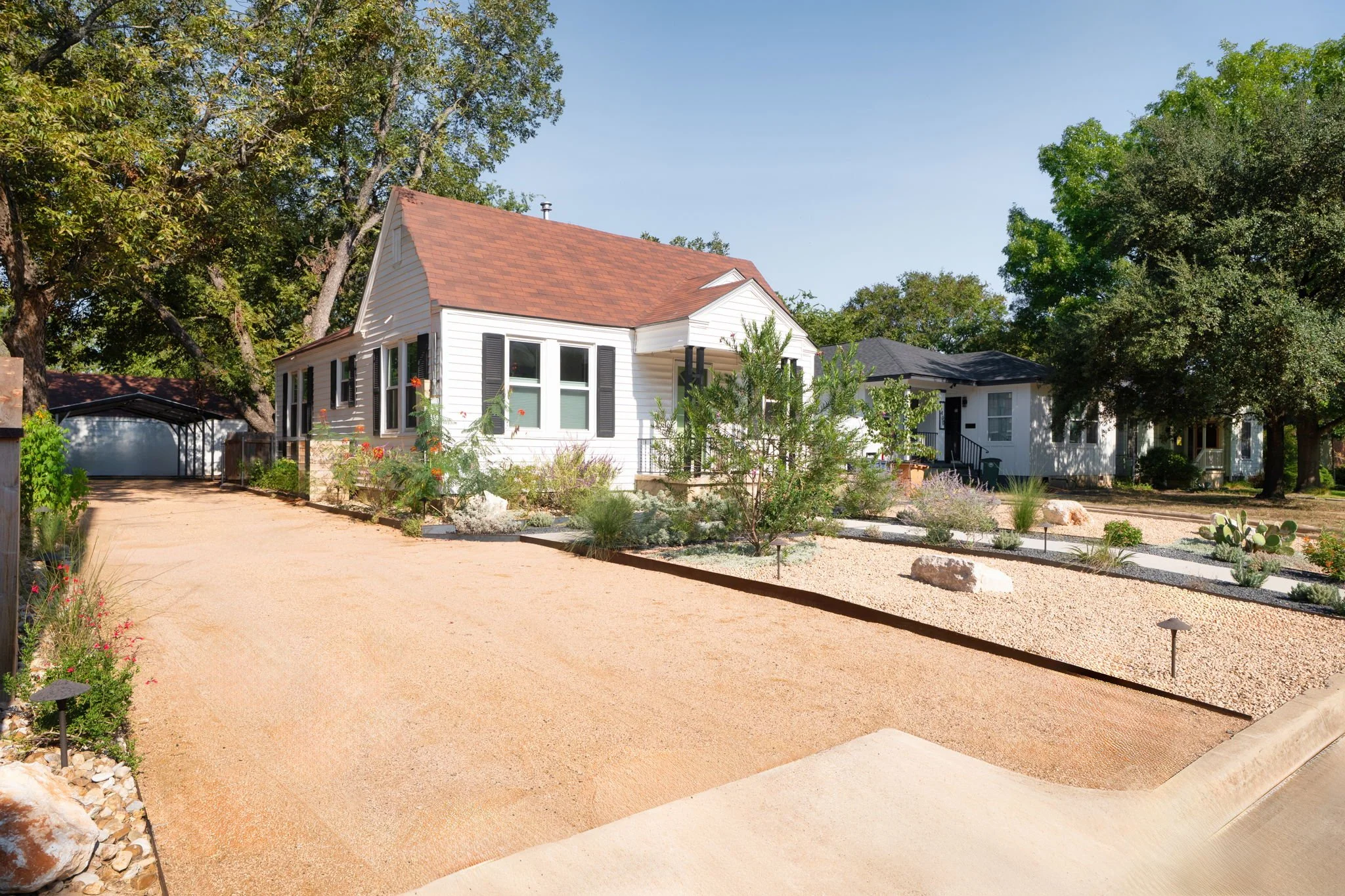 Wide gravel driveway with steel edging and path lighting alongside a low-water native planting bed