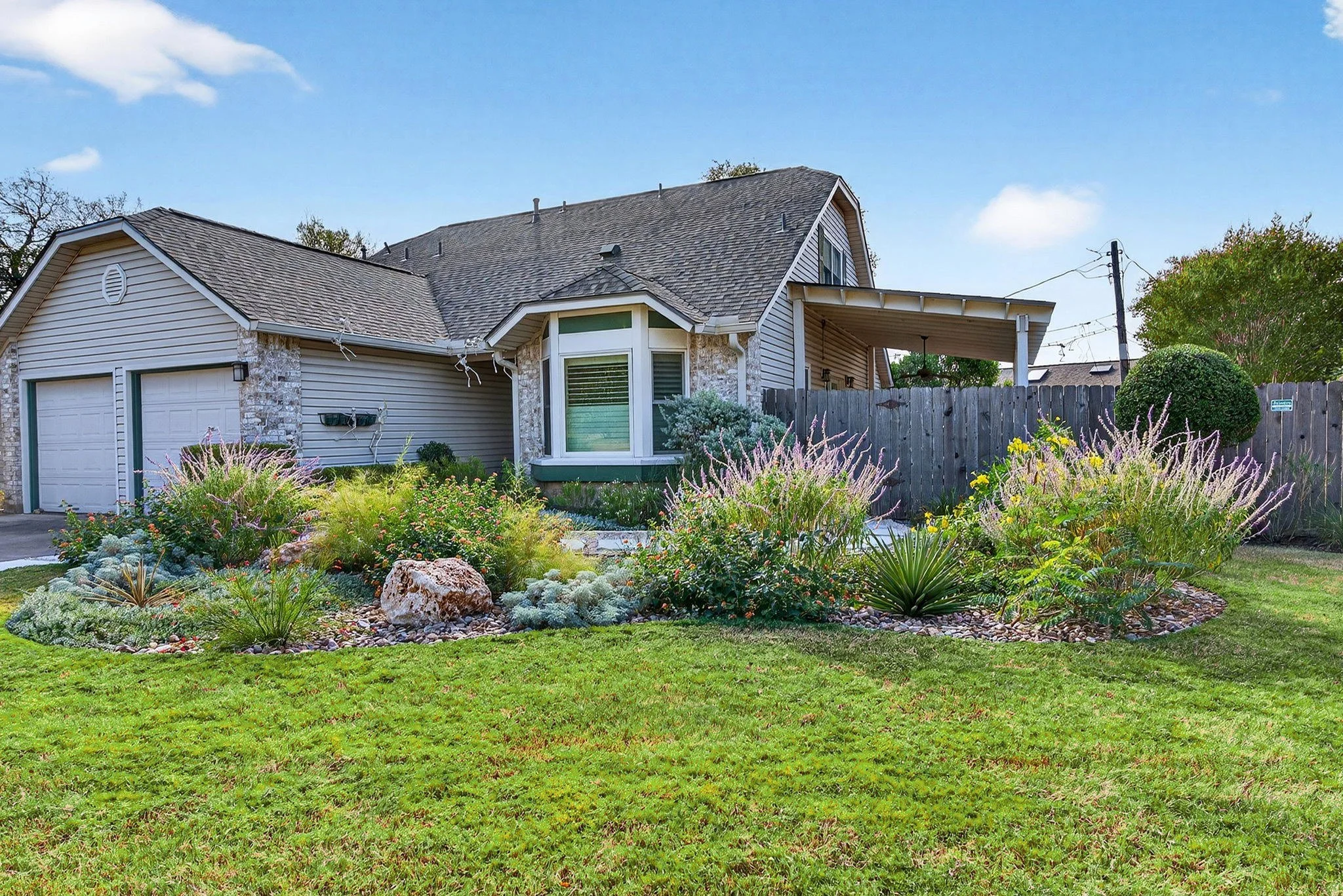 Front elevation with layered perennial beds, boulder accent, and lawn framing the garage and entry