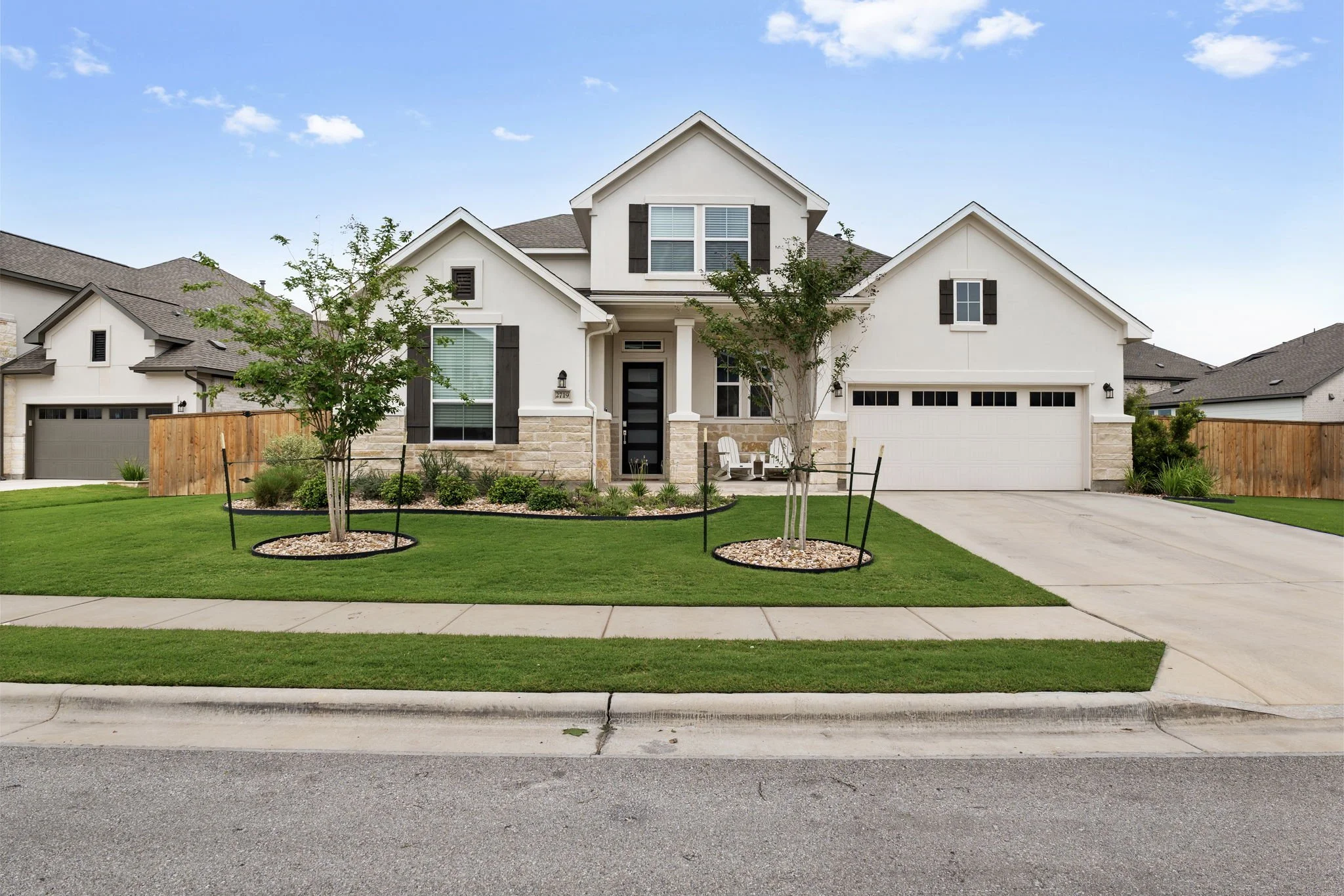 Two-story home with new sod front lawn, staked shade trees in mulch rings, and shrub-lined foundation beds