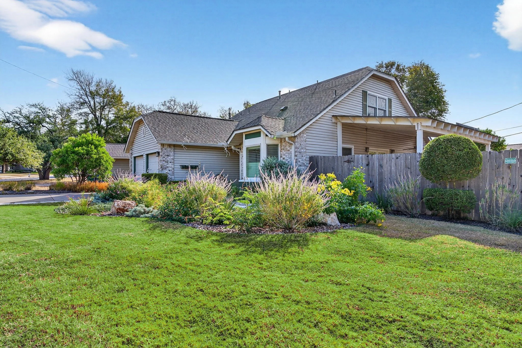 Corner-lot front yard with mixed perennial border, cedar fence, and sculpted evergreen shrub