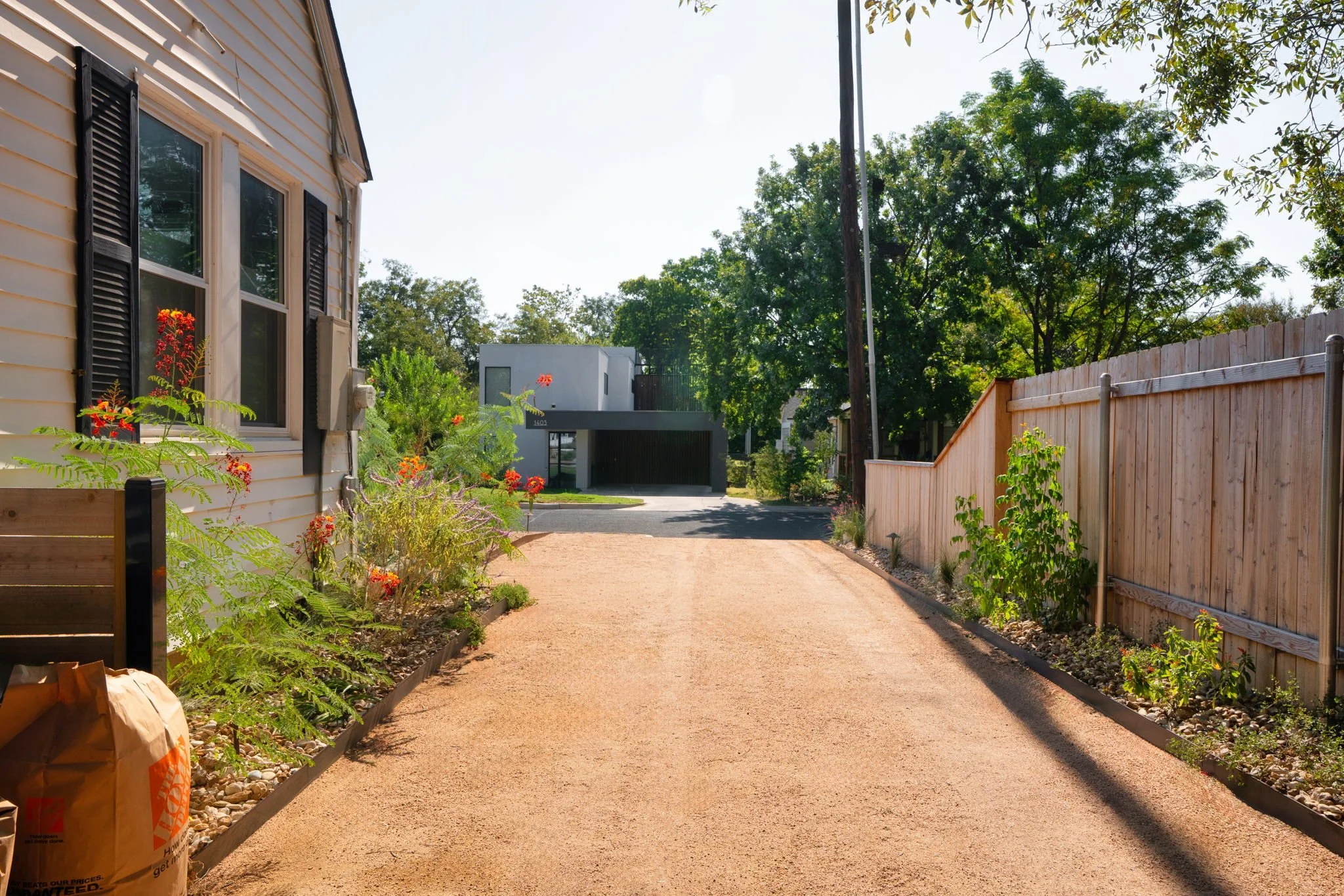 Decomposed granite driveway running between a cottage and cedar privacy fence with native border plantings