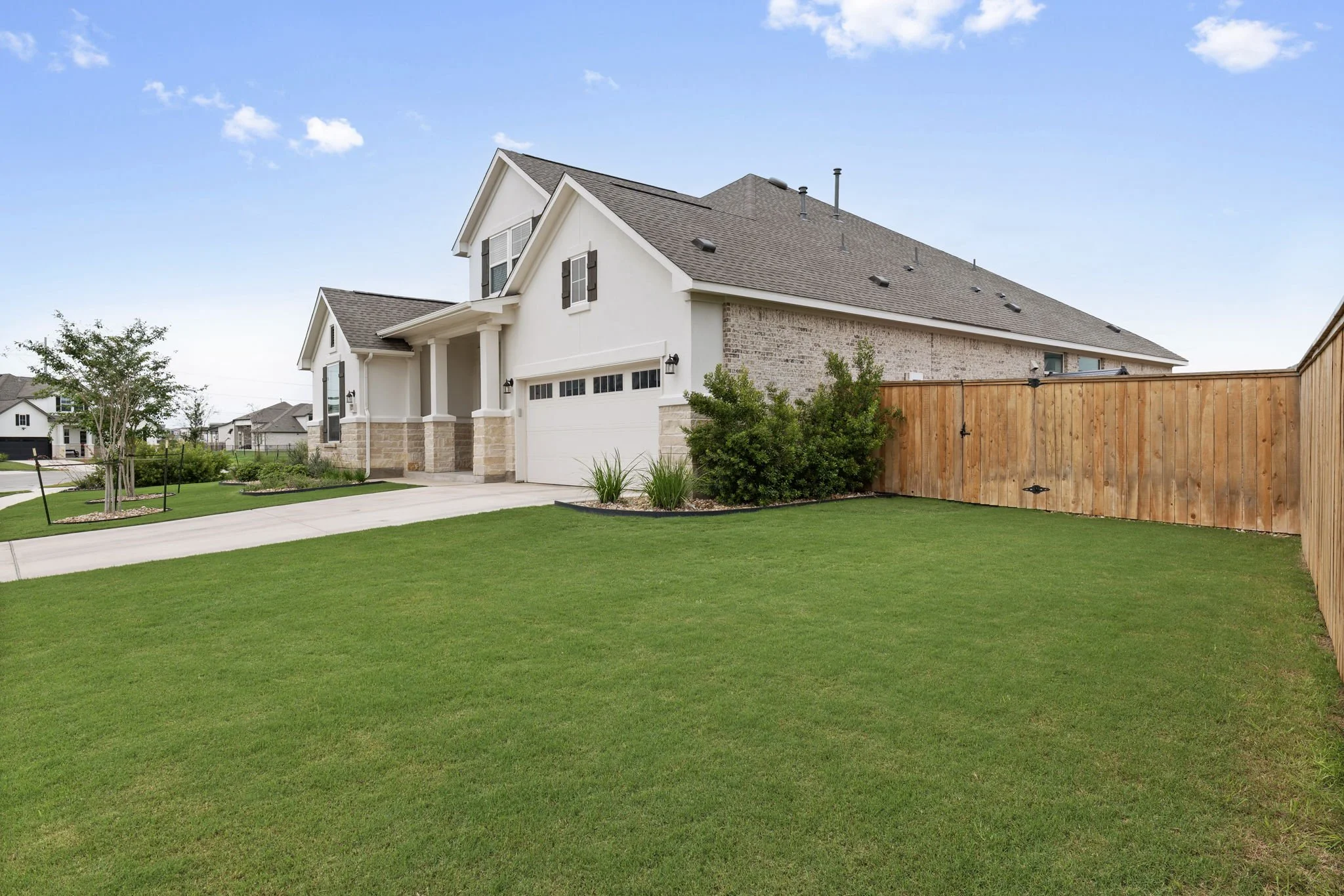 Side yard sod installation with cedar privacy fence, staked ornamental trees, and rock-mulched shrub beds