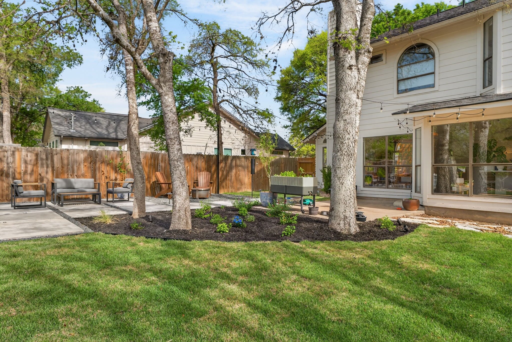 Mature shade trees over a sodded backyard with mulched tree rings, raised planter, and paver patio