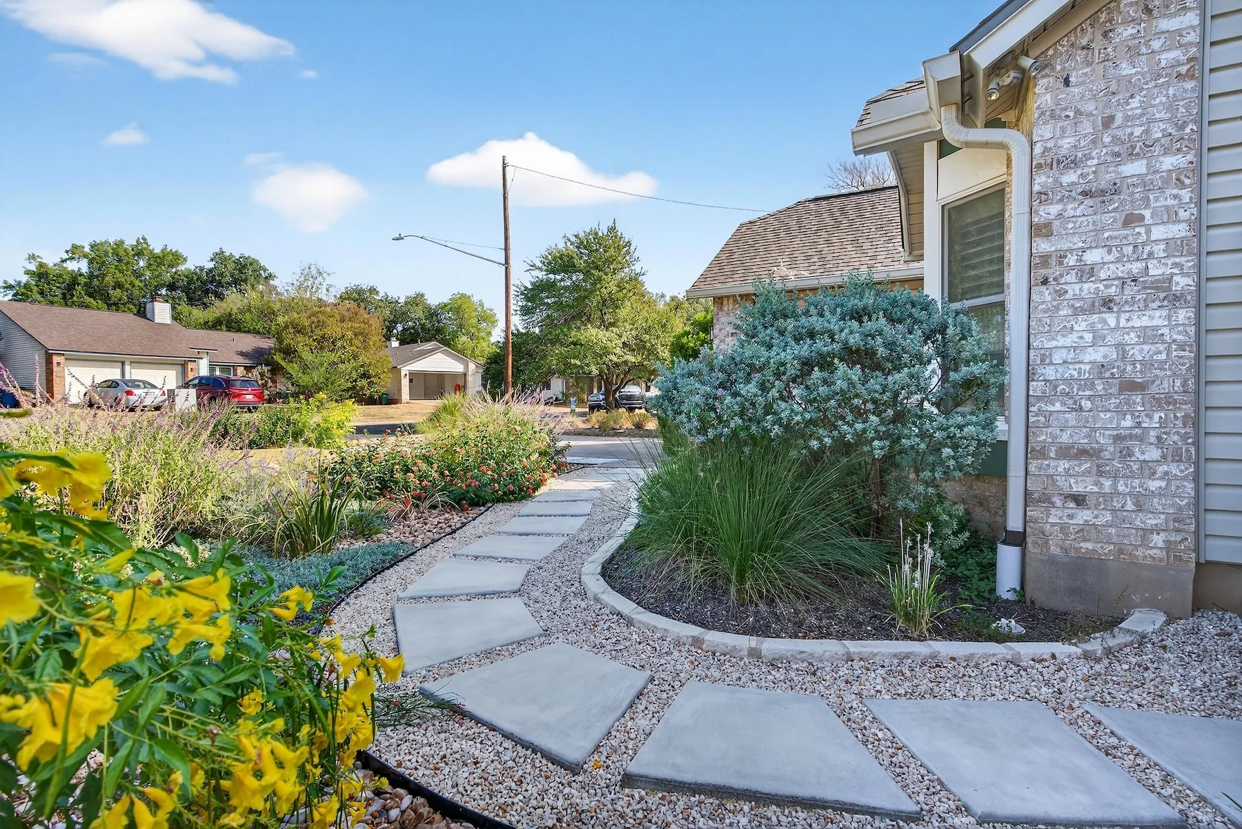 Paver walkway between brick facade and a native bed with agave, silver shrubs, and ornamental grasses