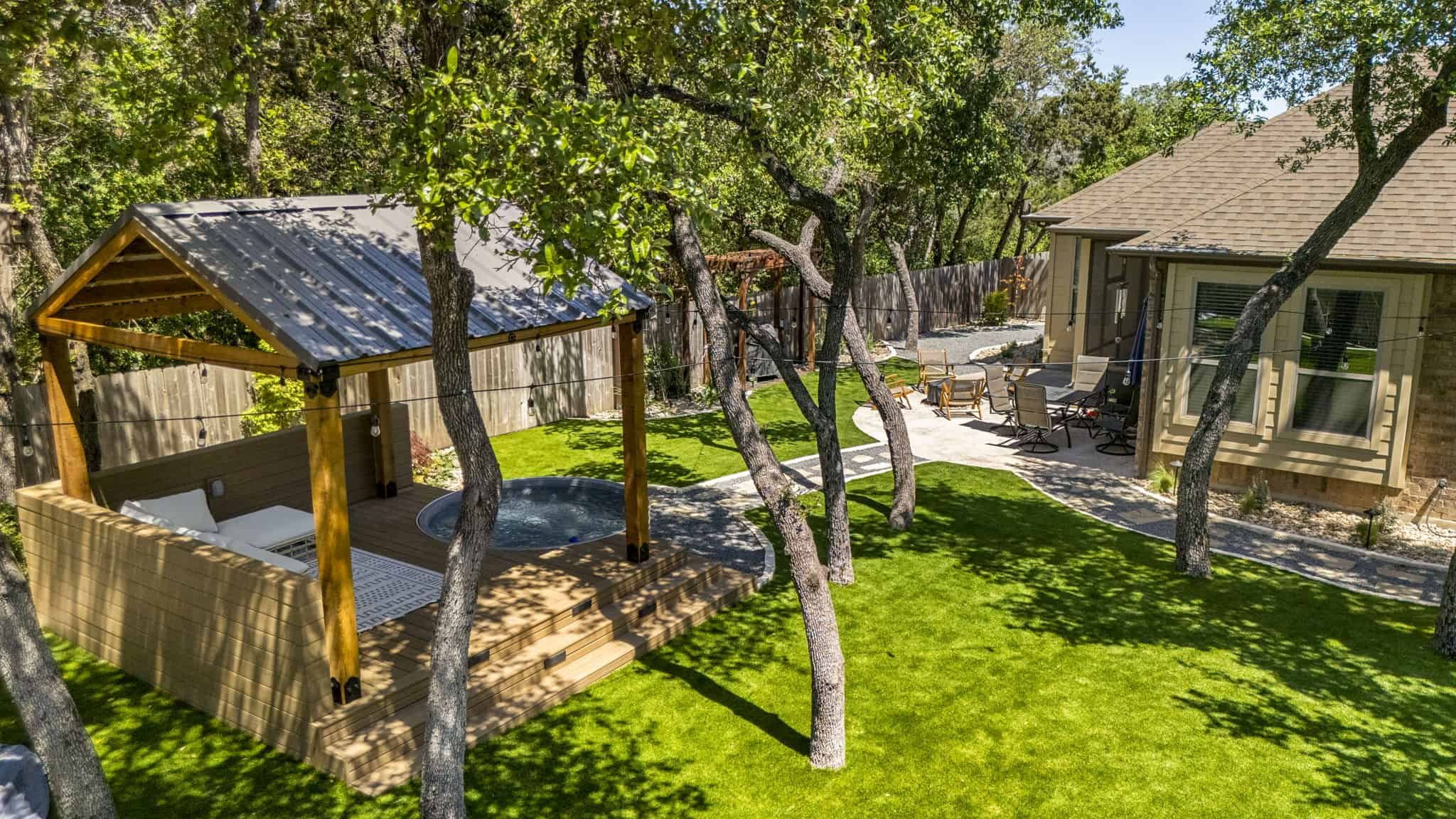Spacious Austin backyard featuring a covered spa patio, shaded by trees, with a nearby fire pit and outdoor dining space.