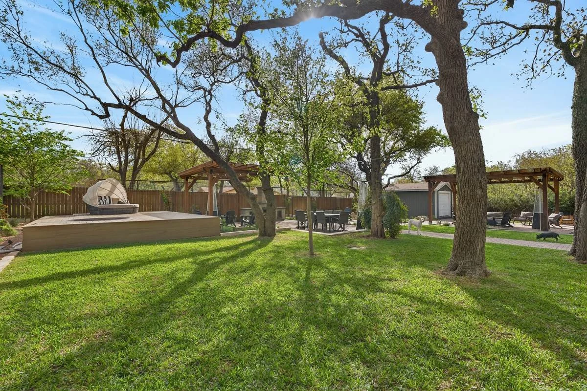 Lawn view of the raised deck with daybed and two cedar pergolas under oaks — Southern Love Landscaping & Design