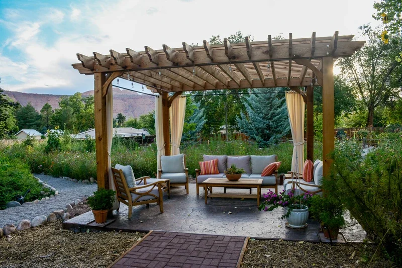Freestanding pergola with curtains and cozy furniture on a patio, highlighting outdoor comfort.