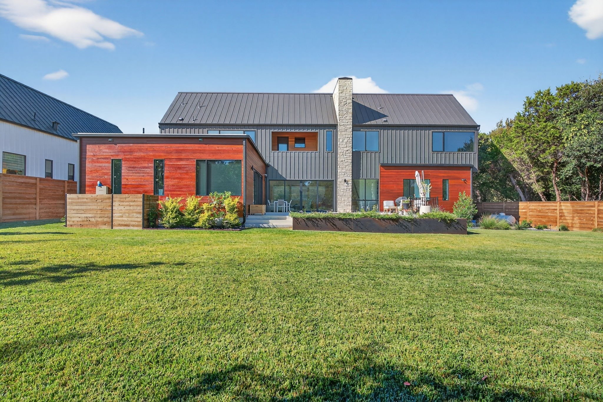 Spacious backyard landscaping with manicured lawn, large planter bed, privacy fencing, and patio seating along a modern home.