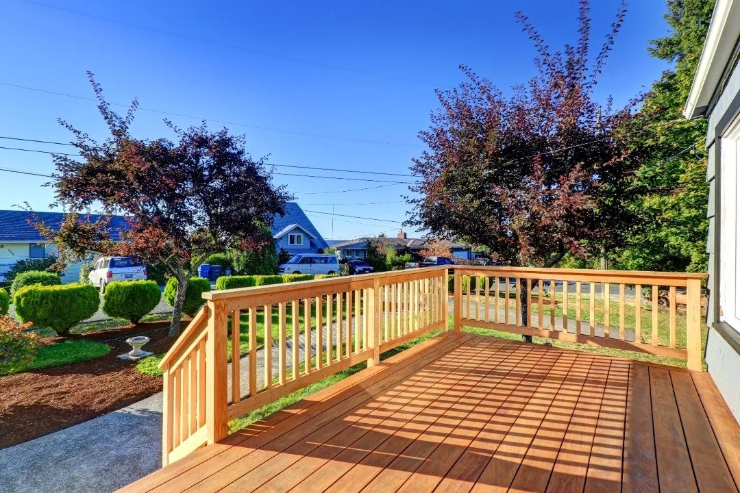 Wooden deck with railings overlooking a landscaped suburban neighborhood, bathed in warm sunlight under a clear blue sky.