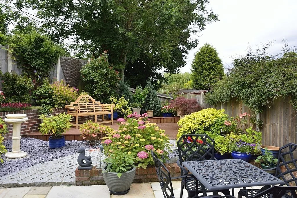 Charming backyard outdoor living space with a wooden bench, vibrant flowers, potted plants, and cozy patio seating.