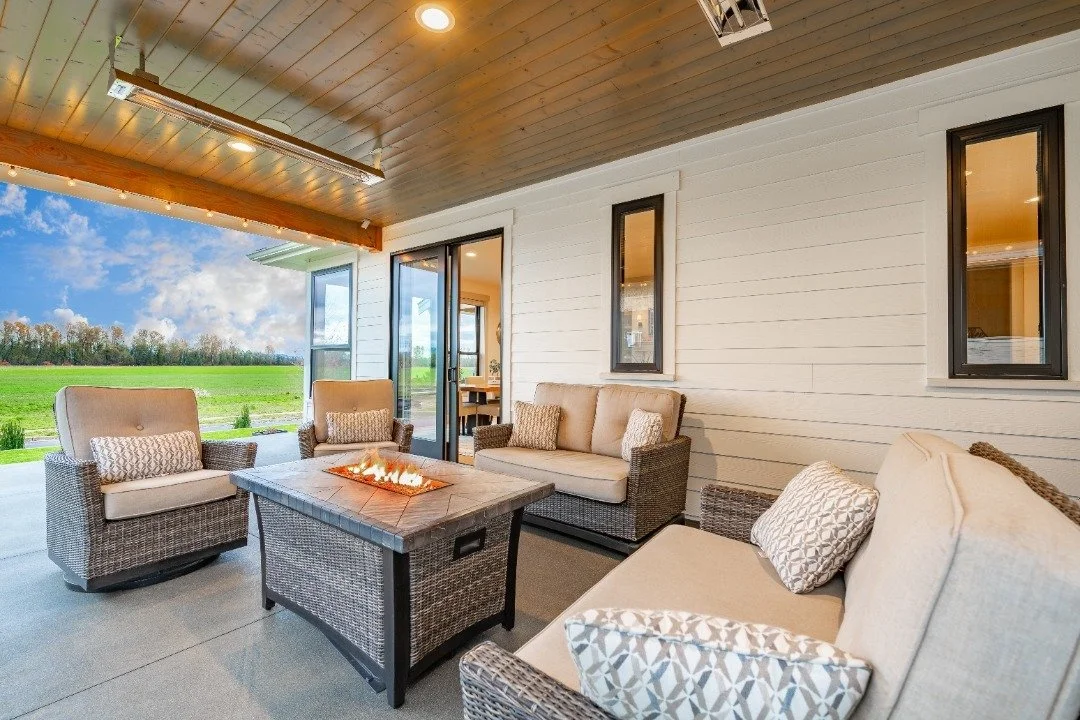 A covered patio with wicker furniture, a fire pit table, and a scenic countryside view, creating a cozy outdoor living space.
