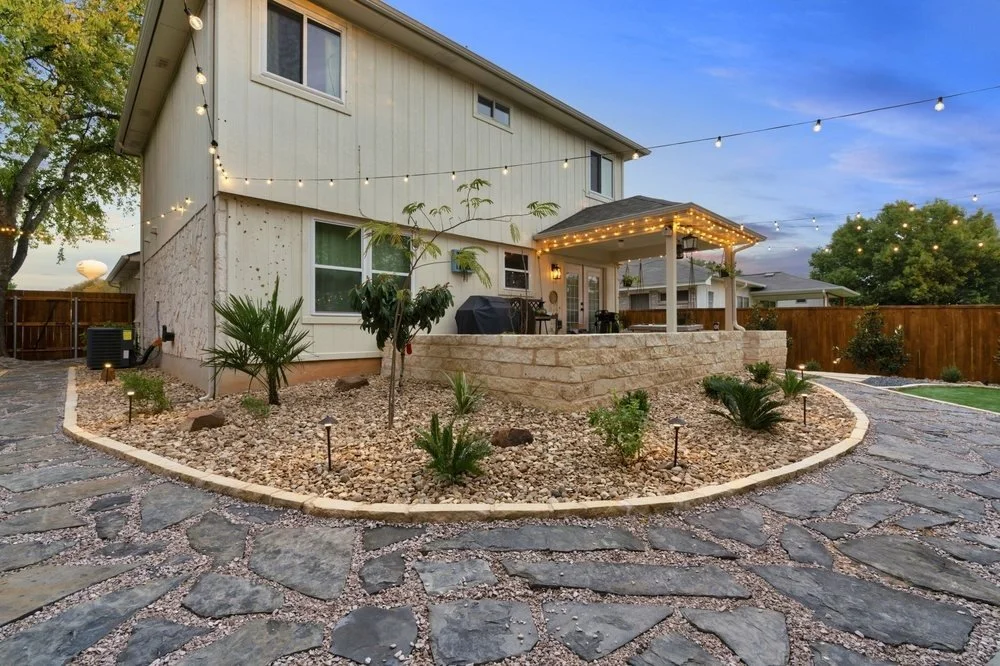Modern backyard with a stone patio, string lights, drought-resistant landscaping, and a covered outdoor seating area at sunset.