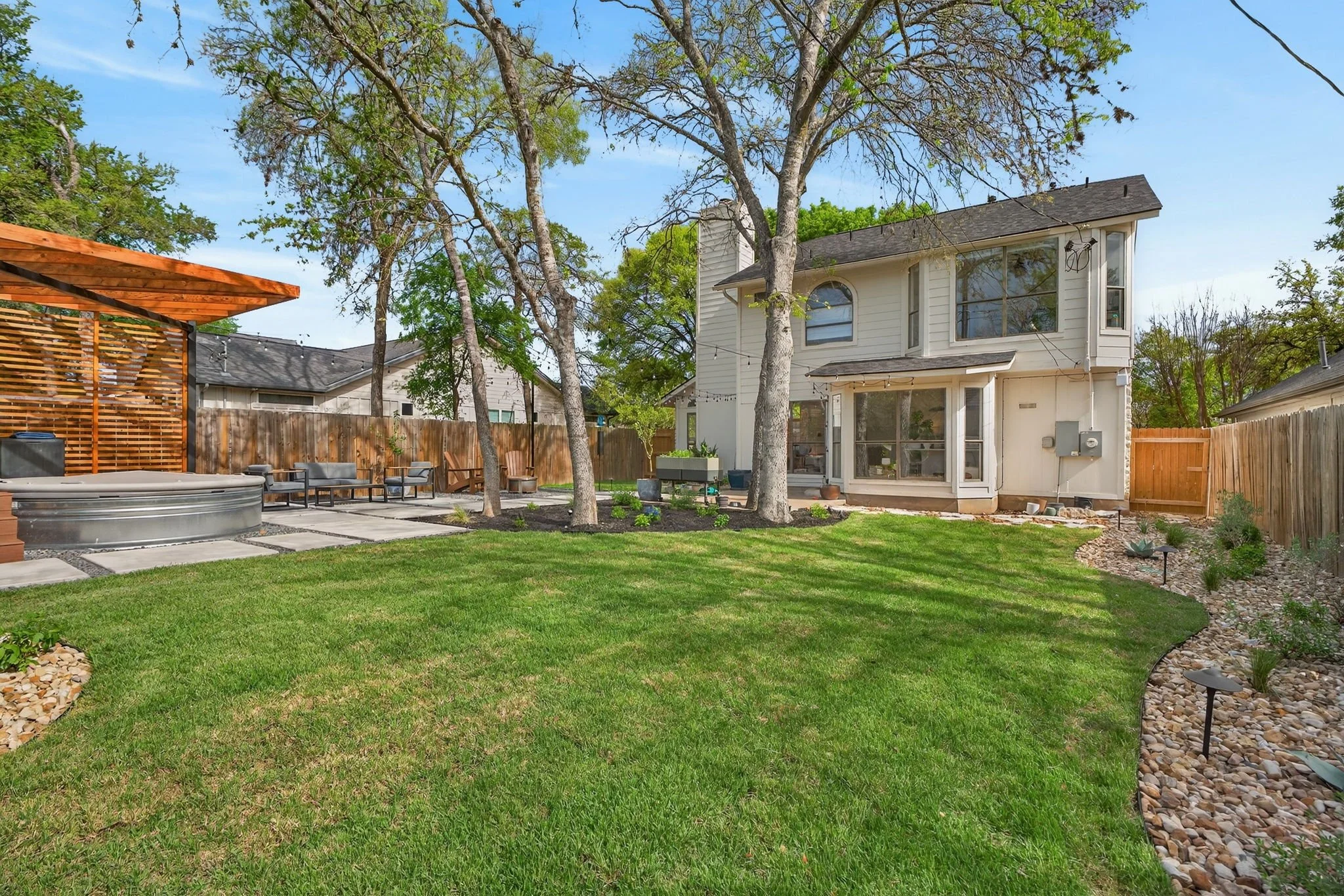 Wide backyard view with fresh sod, curved river rock border, patio lounge seating, and cedar pergola