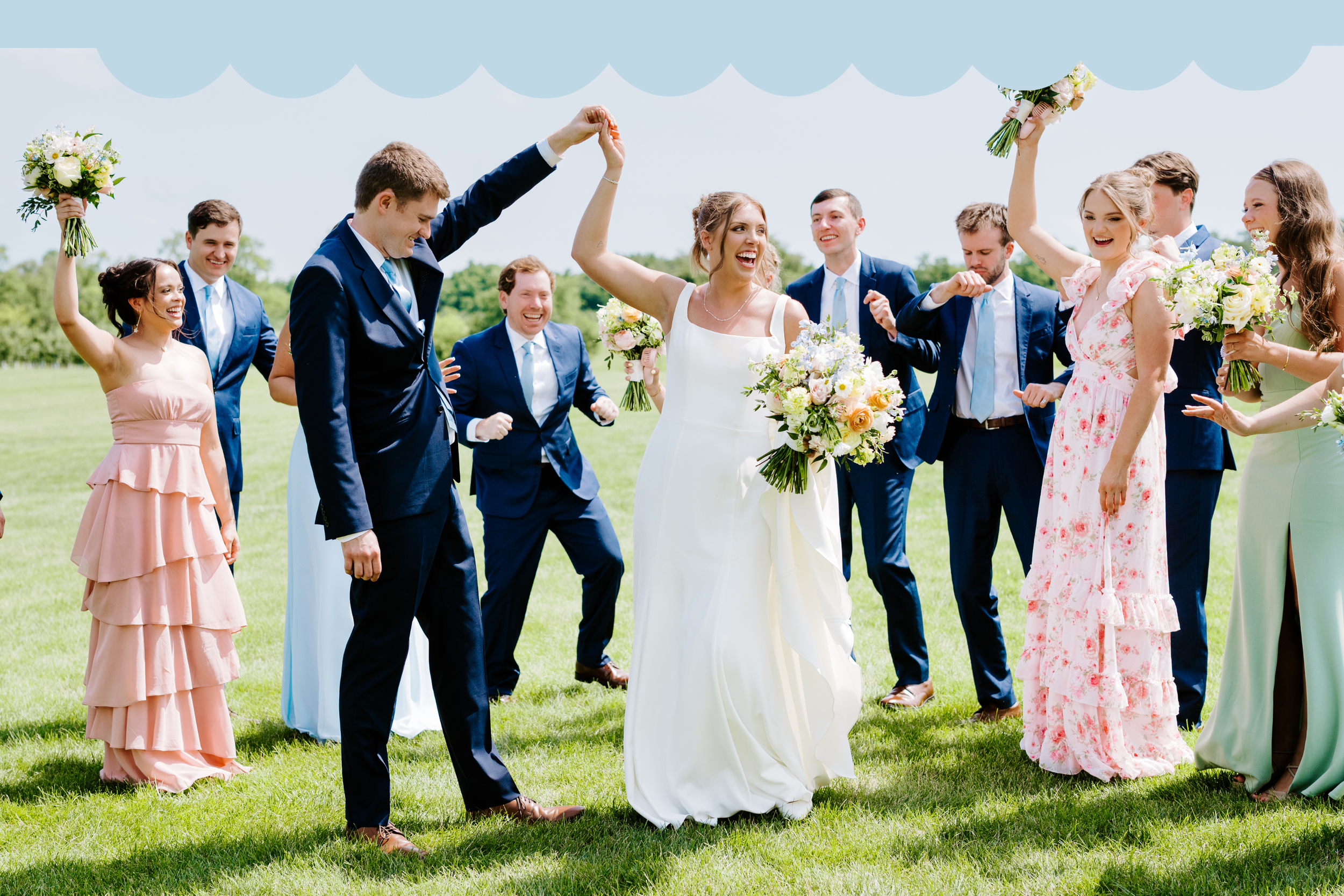 A wedding celebration outdoors with a bride in a white gown and bouquet, surrounded by people in colorful dresses and suits, all smiling and dancing on a grassy field under a cloudy sky.