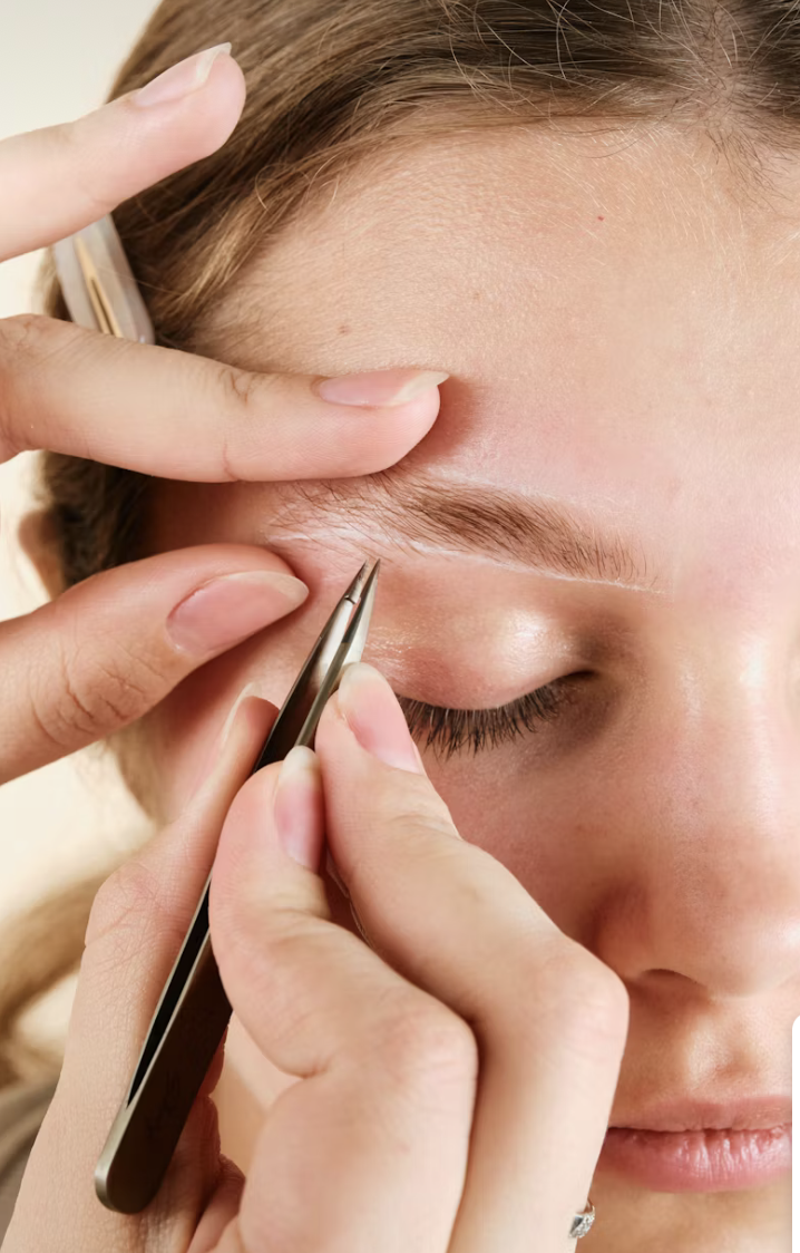 A person getting a beauty treatment or eyebrow grooming using tweezers on their closed eye.