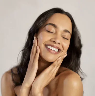 A woman smiling with eyes closed touching her face with both hands.