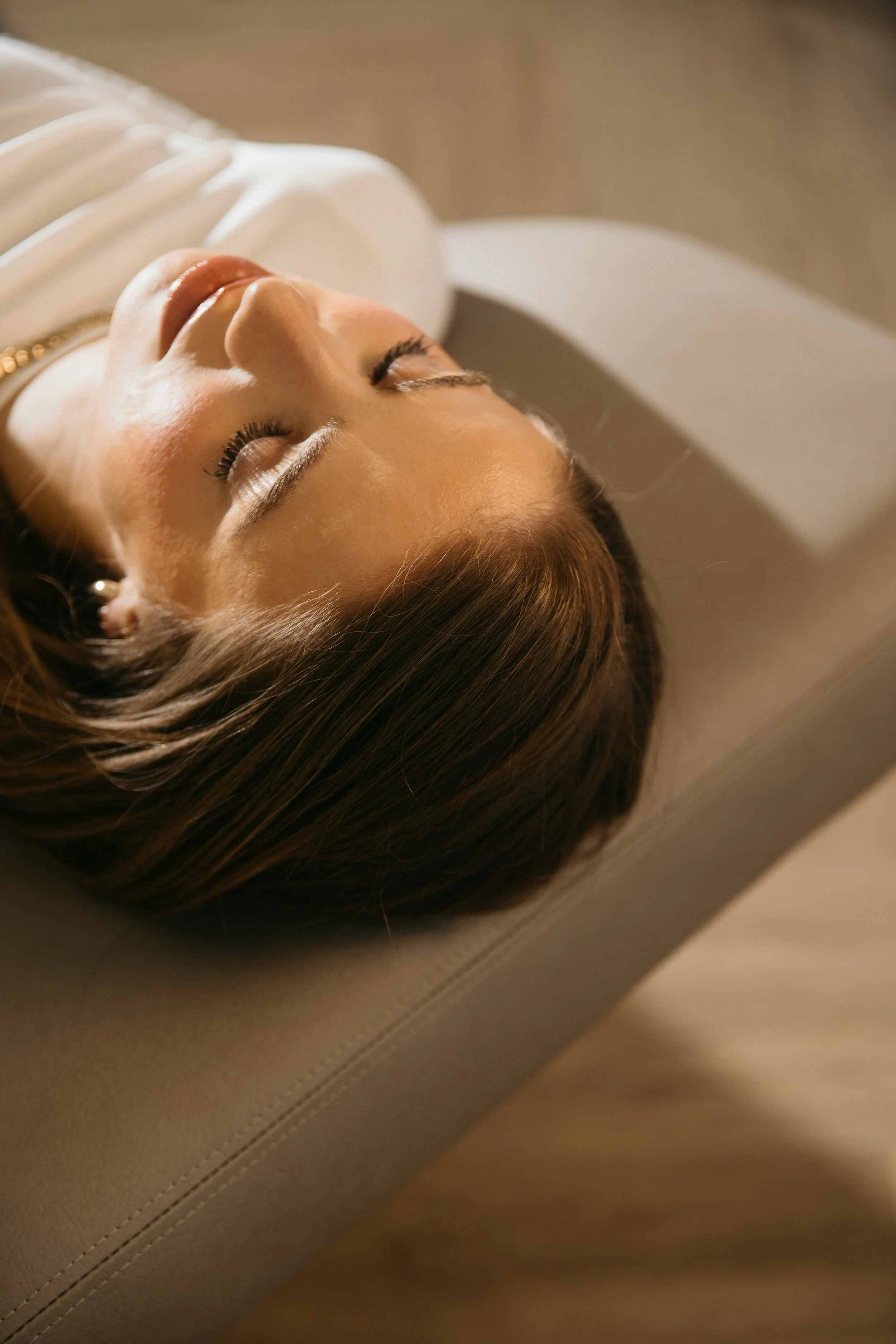 Close-up of a woman with brown hair lying on a couch with her eyes closed, appearing relaxed.
