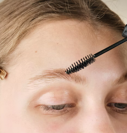 A person applying eyebrow gel with a spoolie brush to their eyebrow.