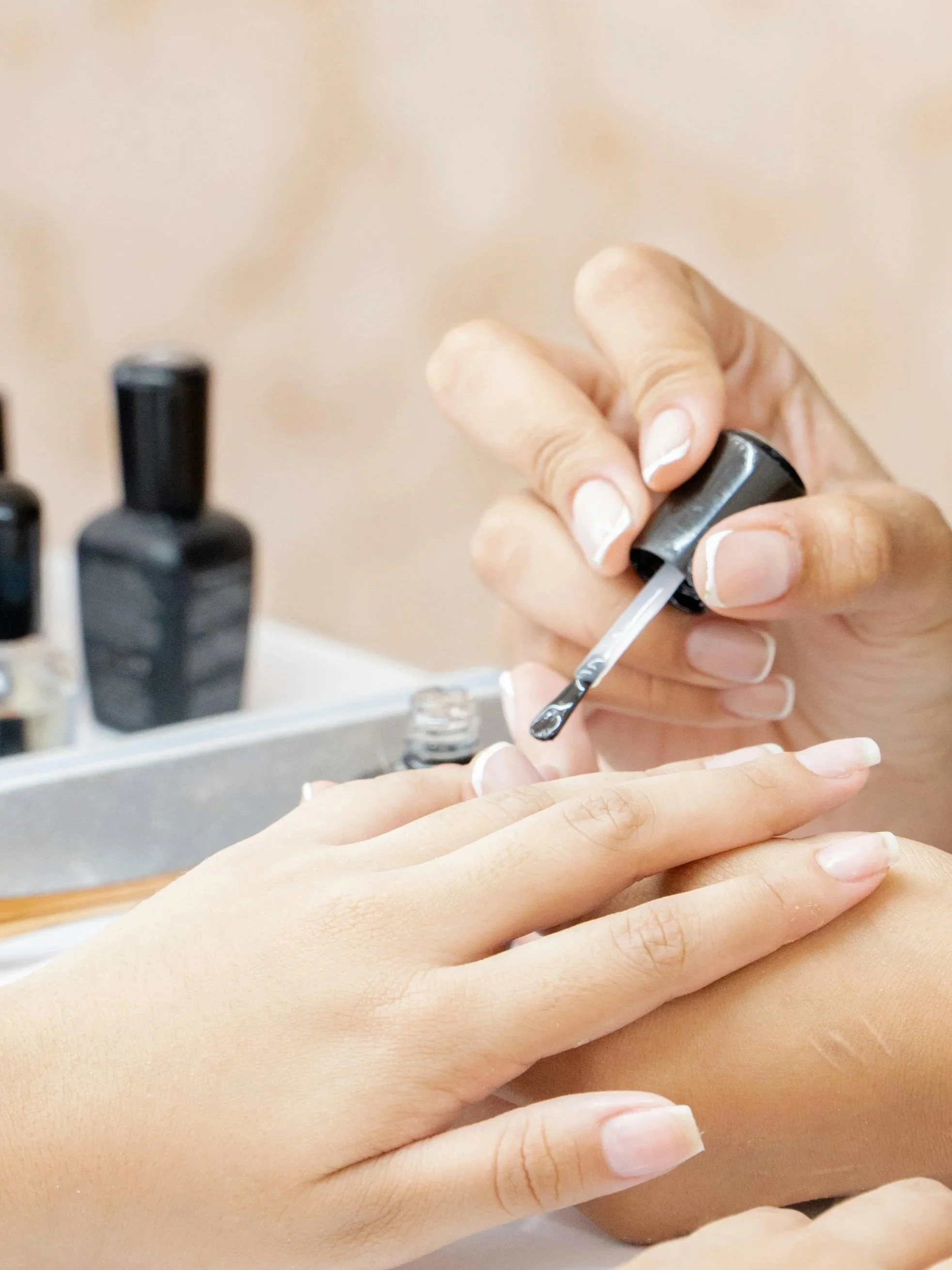 Person applying clear nail polish to another person's fingernails.