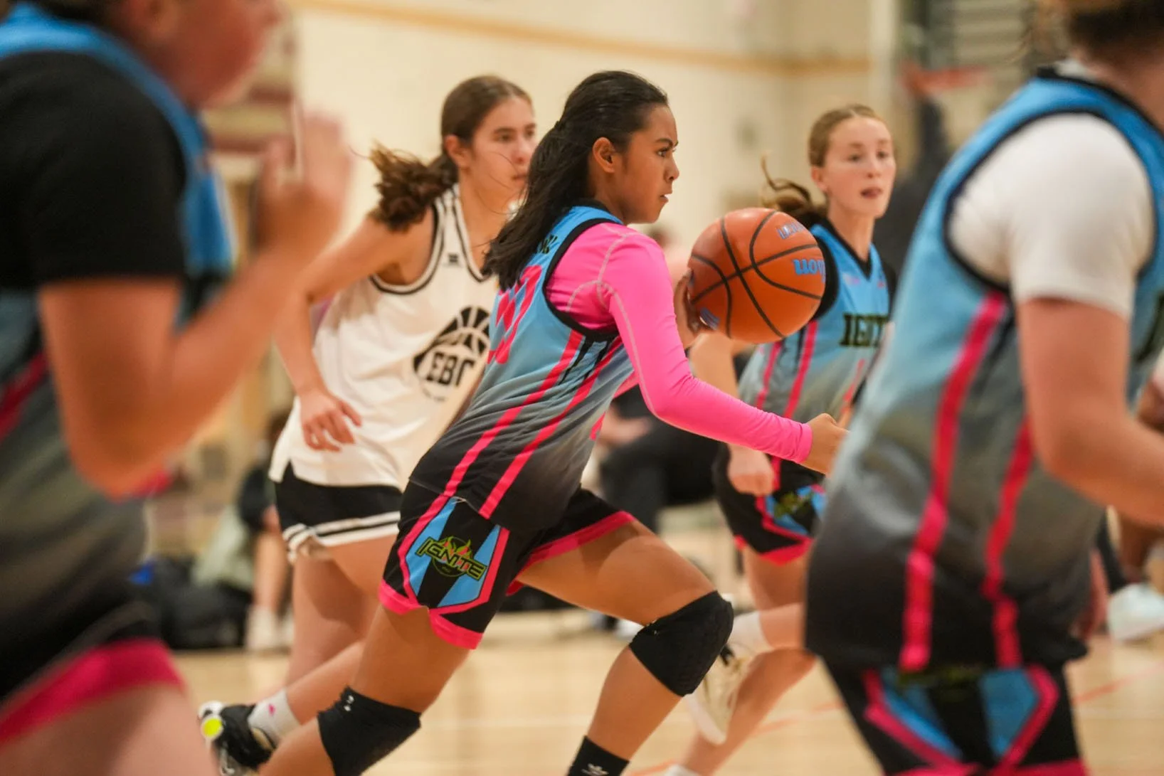Young female basketball player in a pink and blue uniform dribbling a basketball during a game.