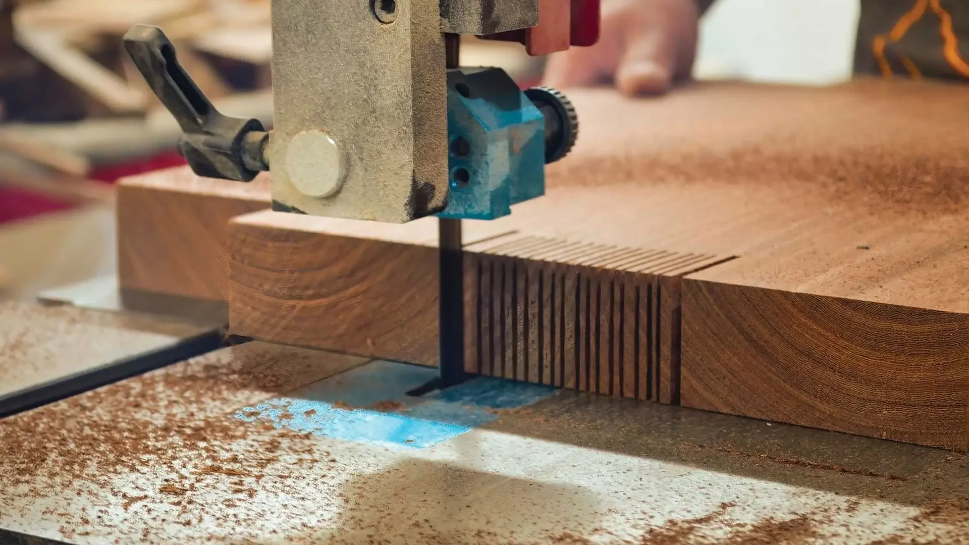 A close-up of a woodworking bandsaw cutting a piece of finished wood, with sawdust scattered on the surface.