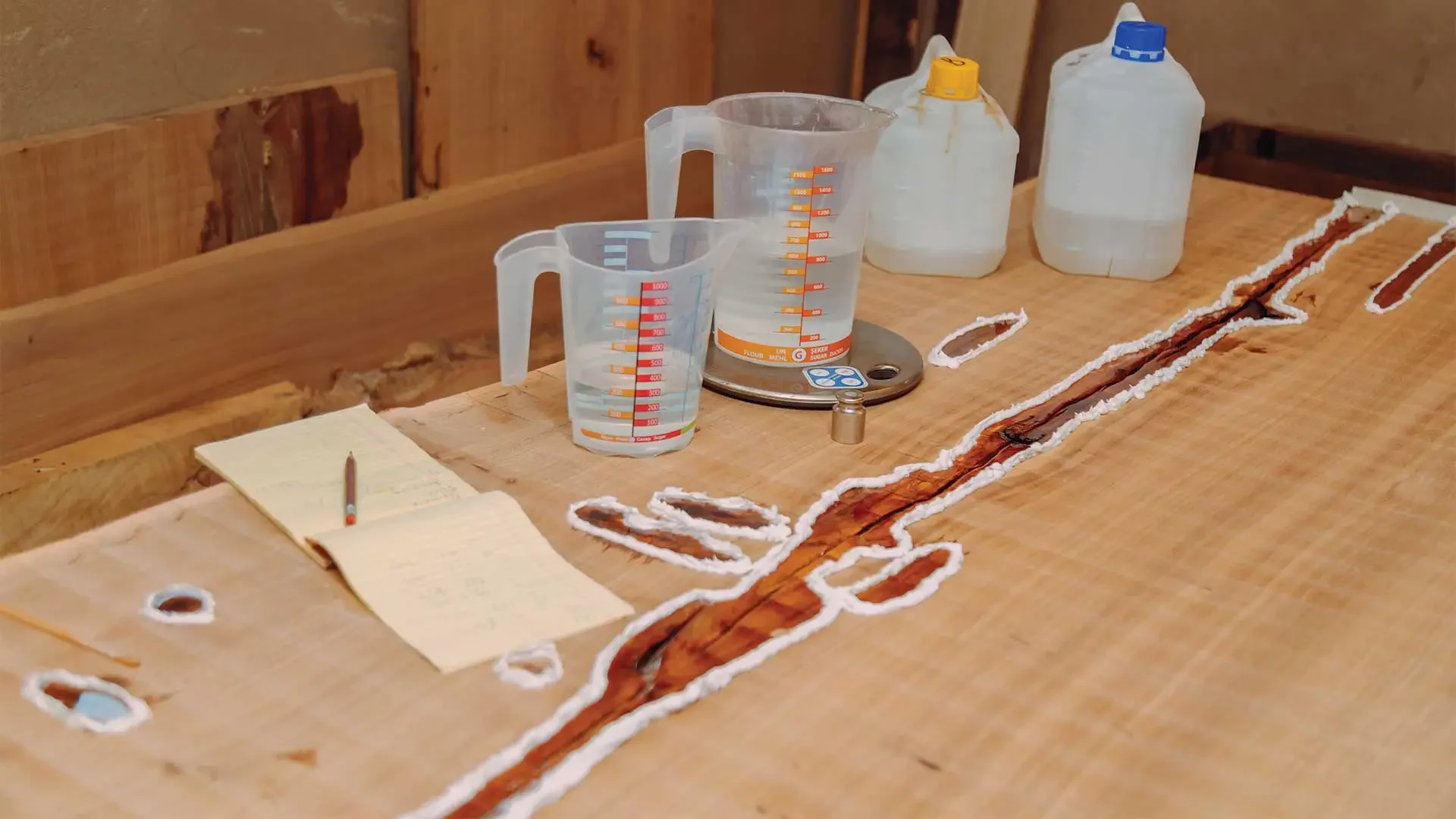 Table with biological sample in a trench on wood surface, measuring cups, a notebook, and bottles of liquids, possibly in a scientific or archaeological setting.
