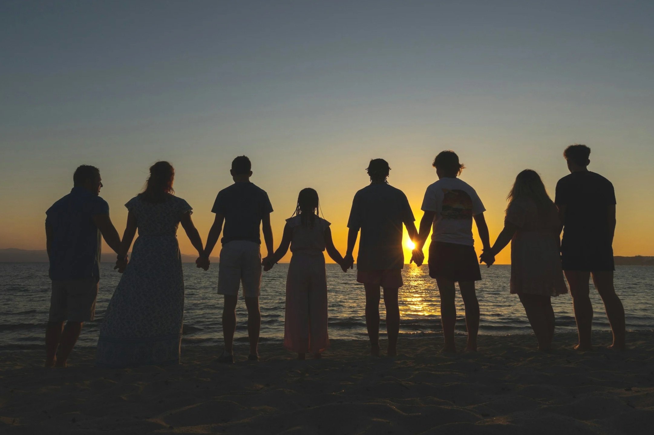 Group of people holding hands on the beach during sunset.