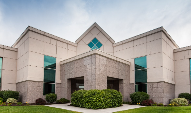 Exterior of a modern office building with large windows and landscaped bushes and grass in front.