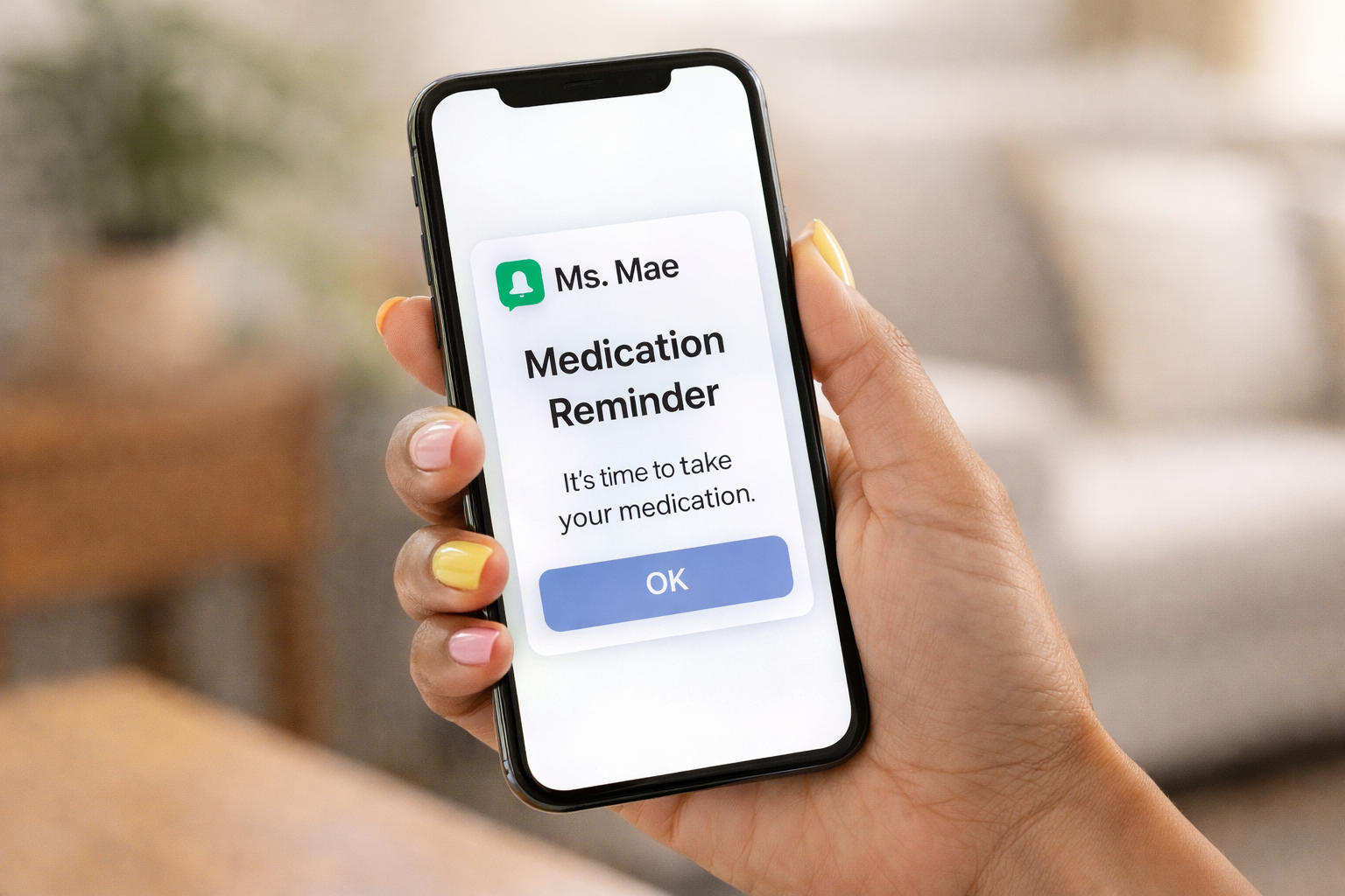 A hand holding a smartphone displaying a medication reminder alert from Ms. Mae with a message to take medication and an OK button.