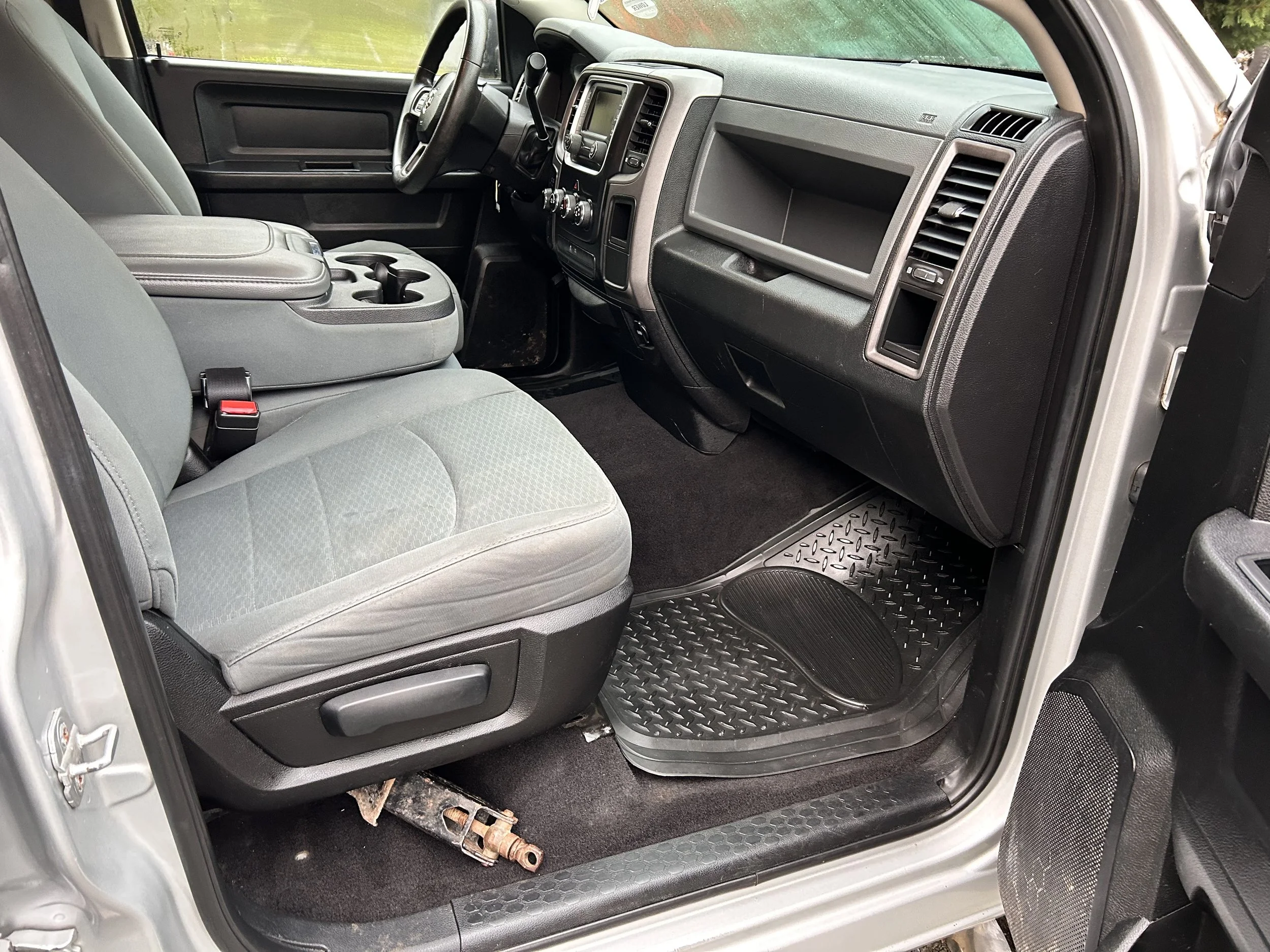 Inside of a vehicle showing the driver's seat, passenger seat, dashboard with vents and controls, and floor mats.