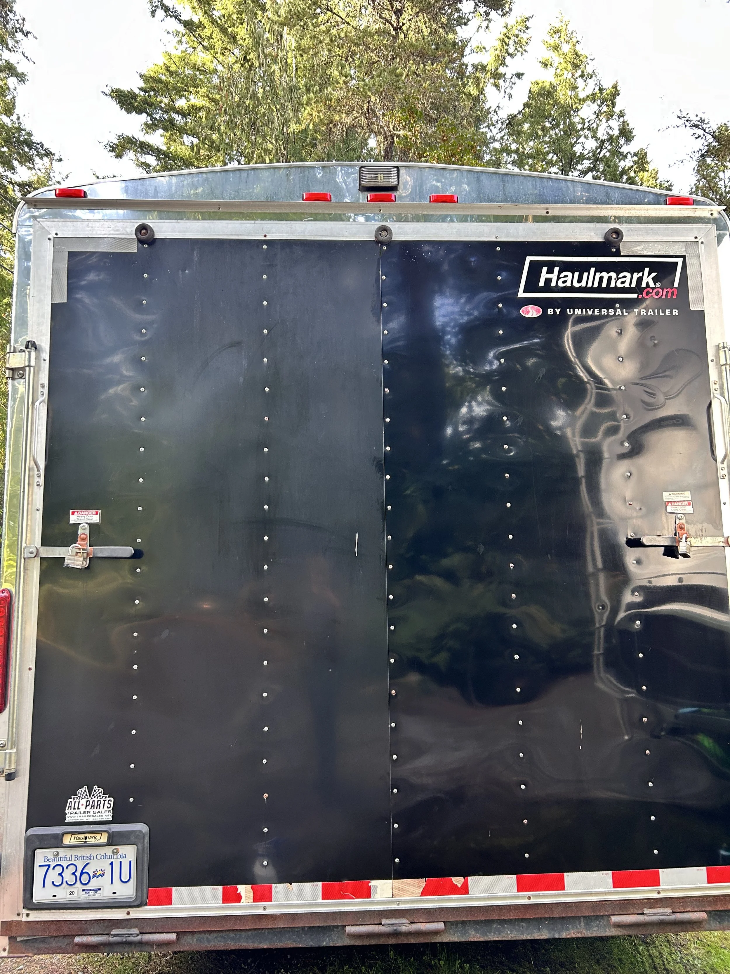 Rear view of a black Haulmark trailer with a Canadian license plate, surrounded by trees.