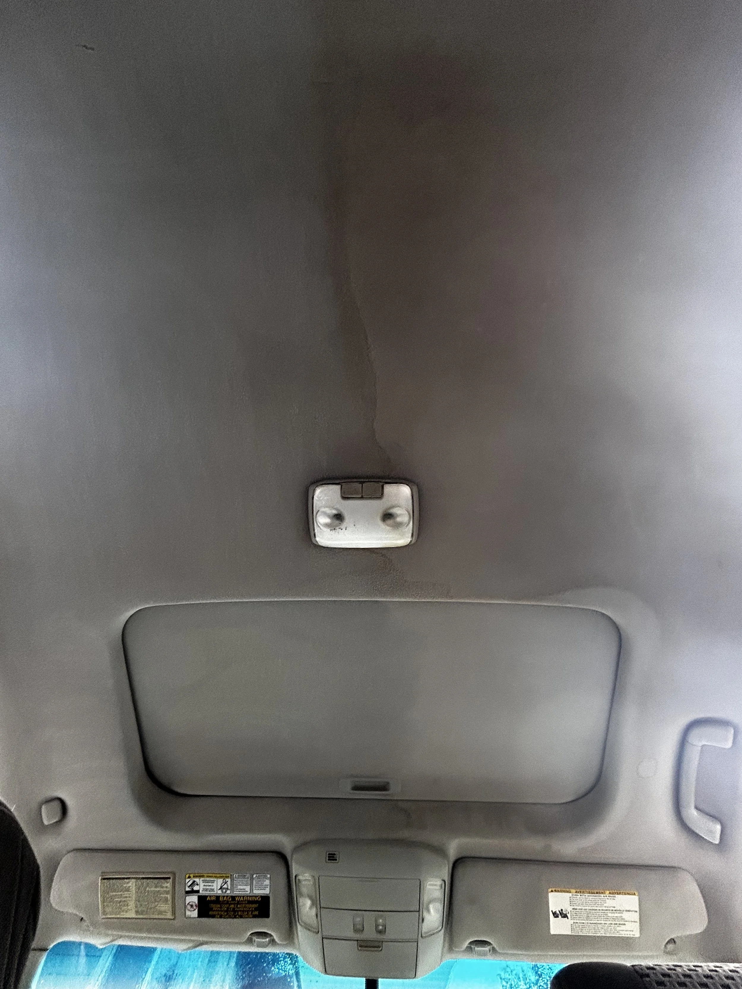 View of a car's interior ceiling, including a rectangular overhead console, reading lights, and sun visors.