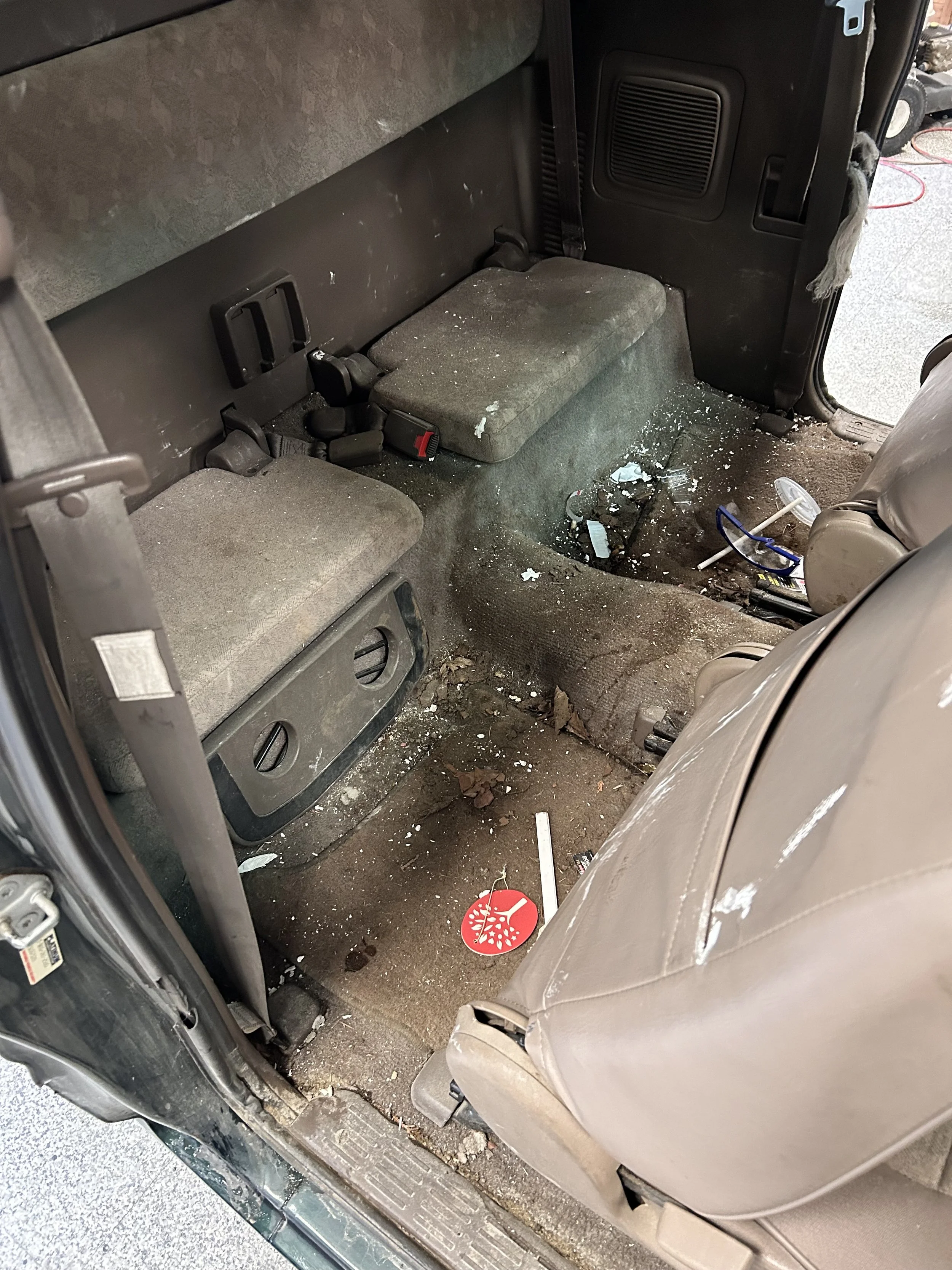 Dirty and messy backseat interior of a vehicle with trash, soda spill, and debris on the floor and seats.