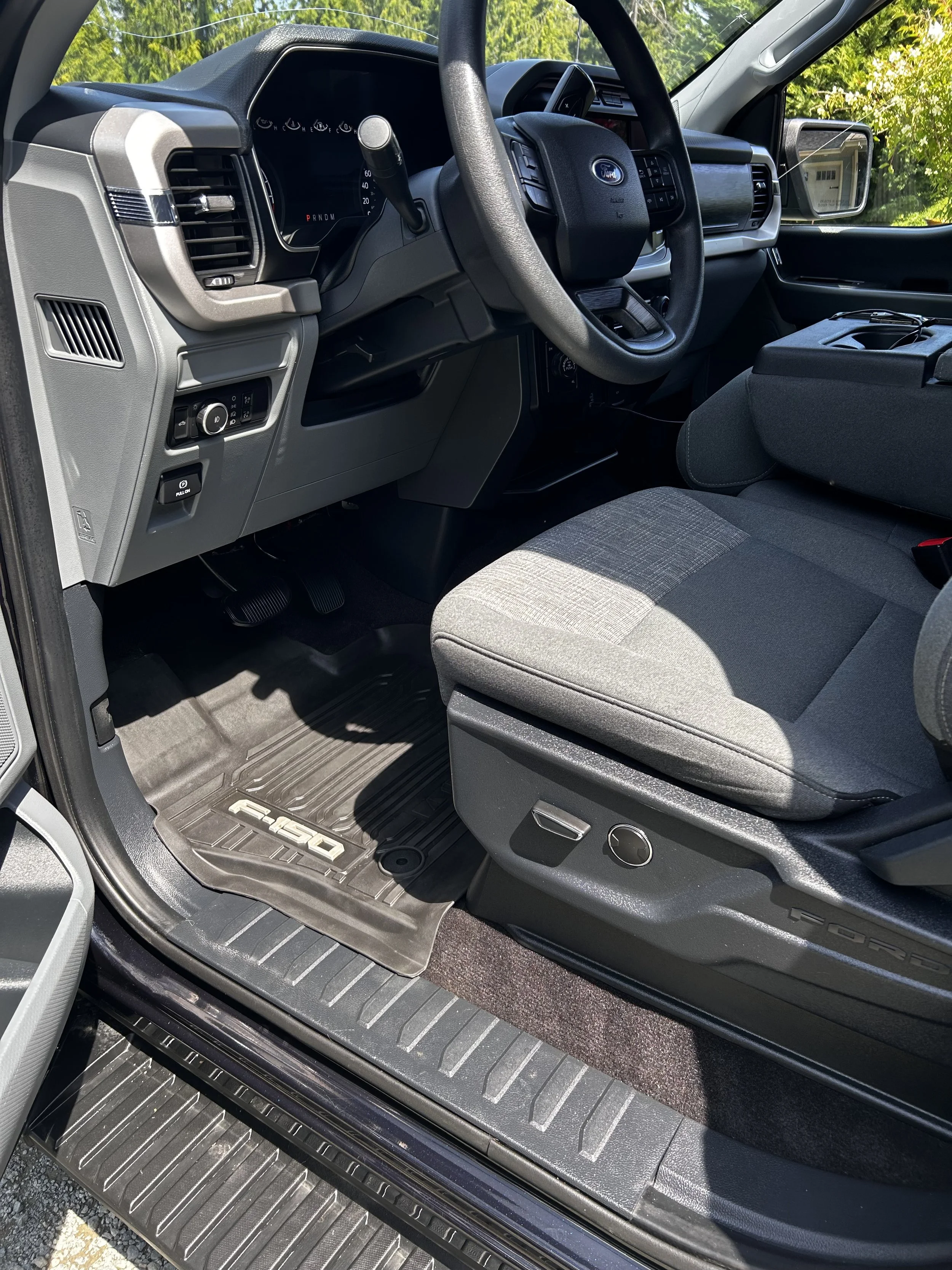 Interior view of a Ford F-150 truck's driver's seat and dashboard, including steering wheel, gear shift, and floor mat.