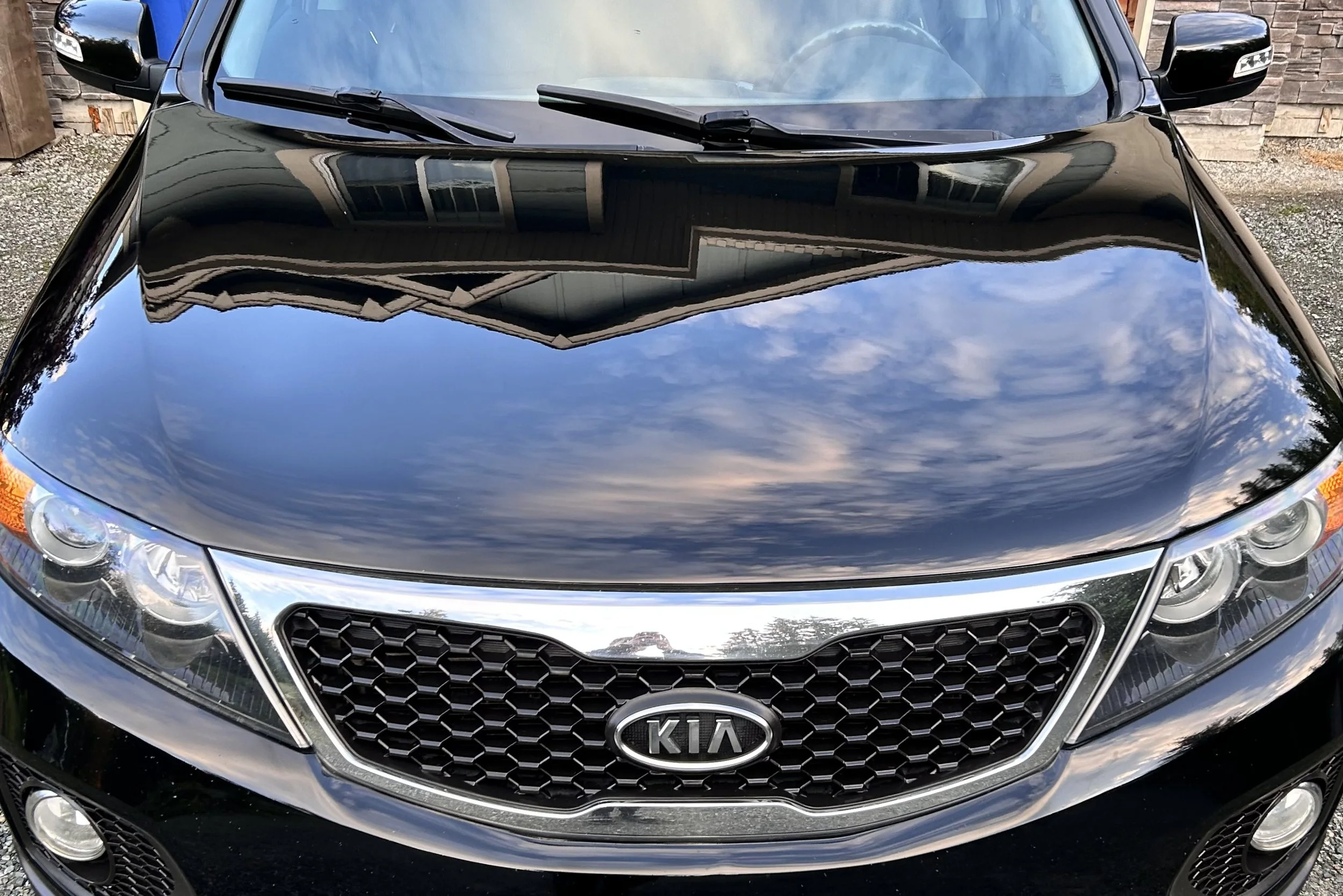 Front view of a black Kia car with reflection of the sky and clouds on the hood.