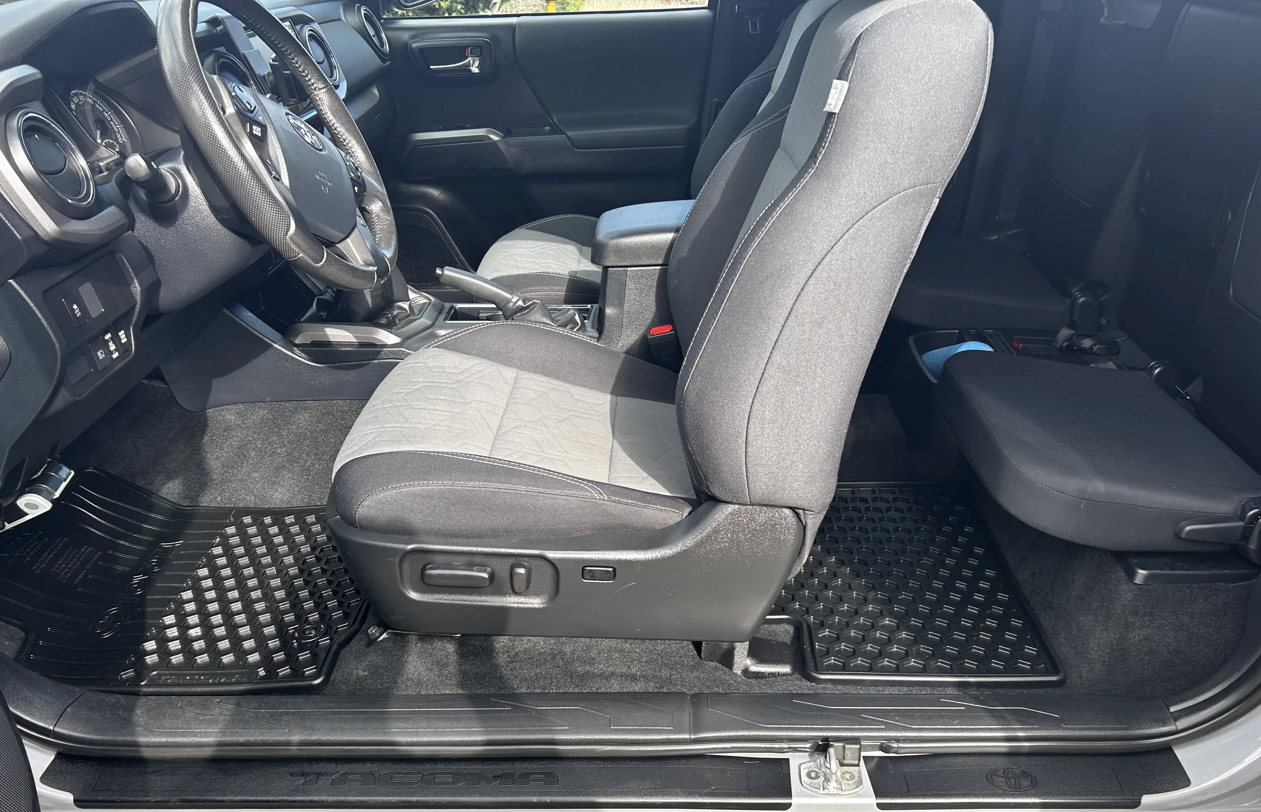 Interior of a Toyota Tacoma, showing the front driver and passenger seats, dashboard, steering wheel, gear shift, and floor mats.