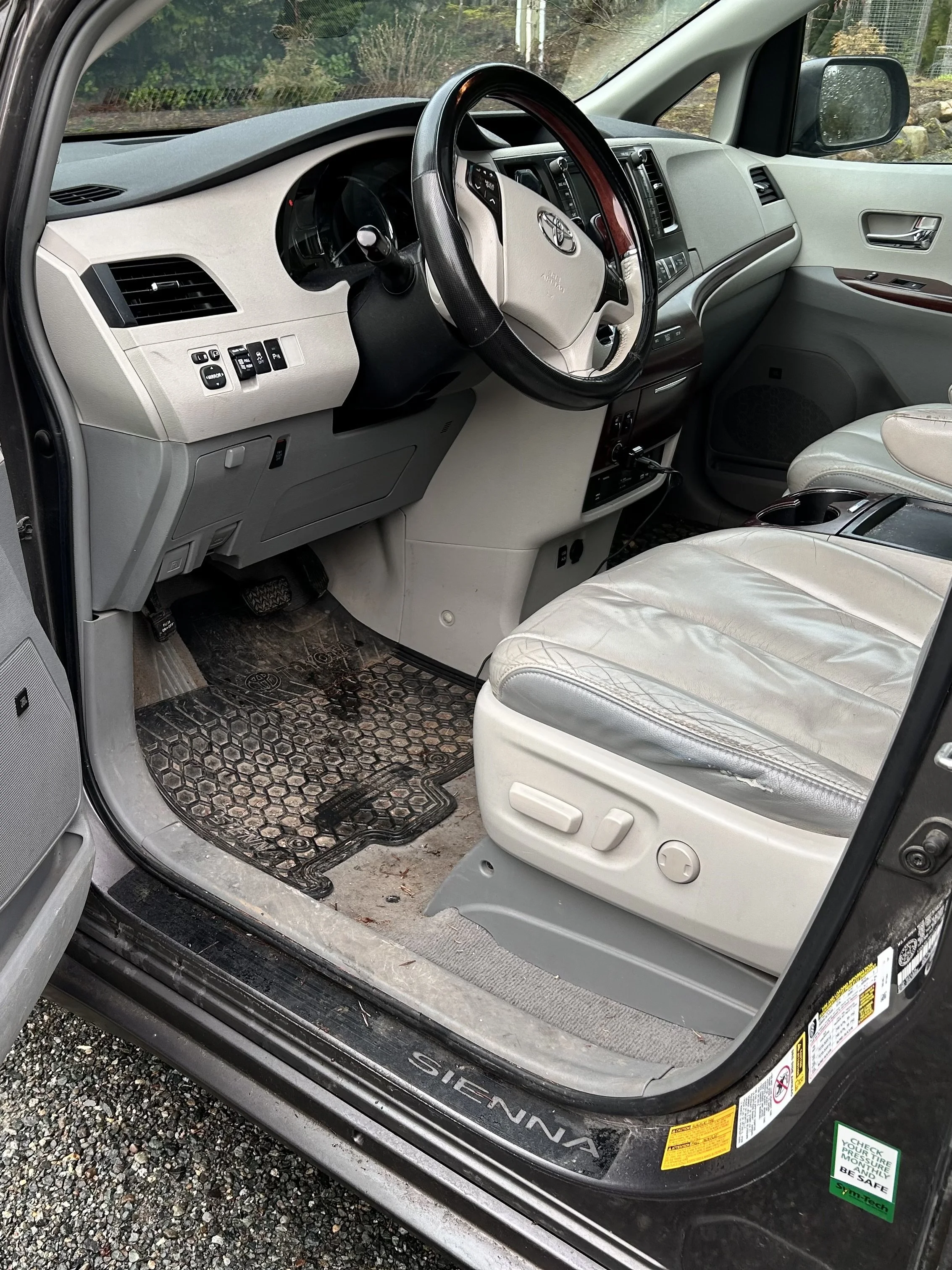 Interior of a beige Toyota Sienna minivan showing the driver’s seat, dashboard, steering wheel, and front passenger seat, with dirt and wear on the floor mats and seat.