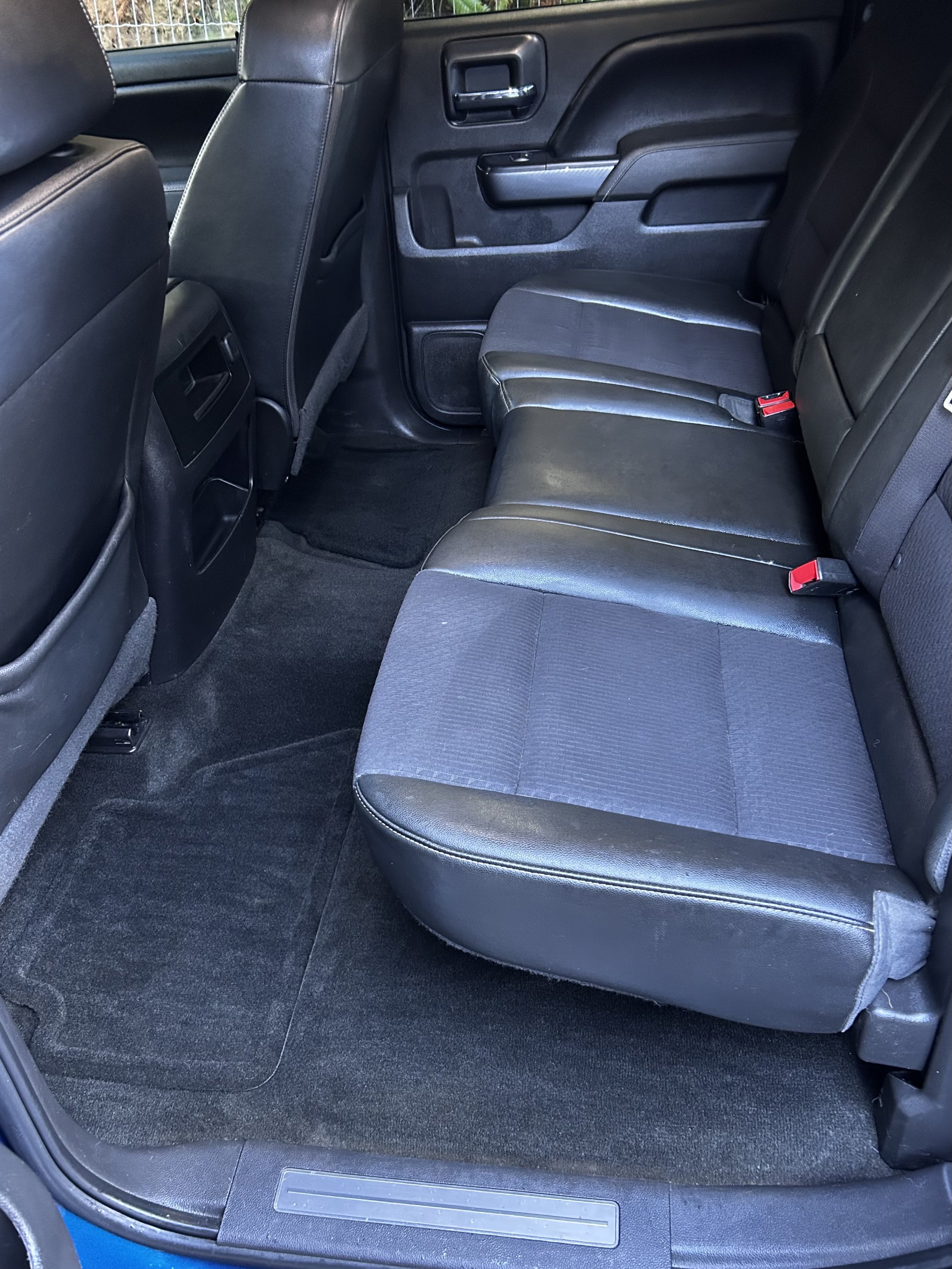 The back seat interior of a black vehicle with black leather seats, black carpet, and a black door panel visible.