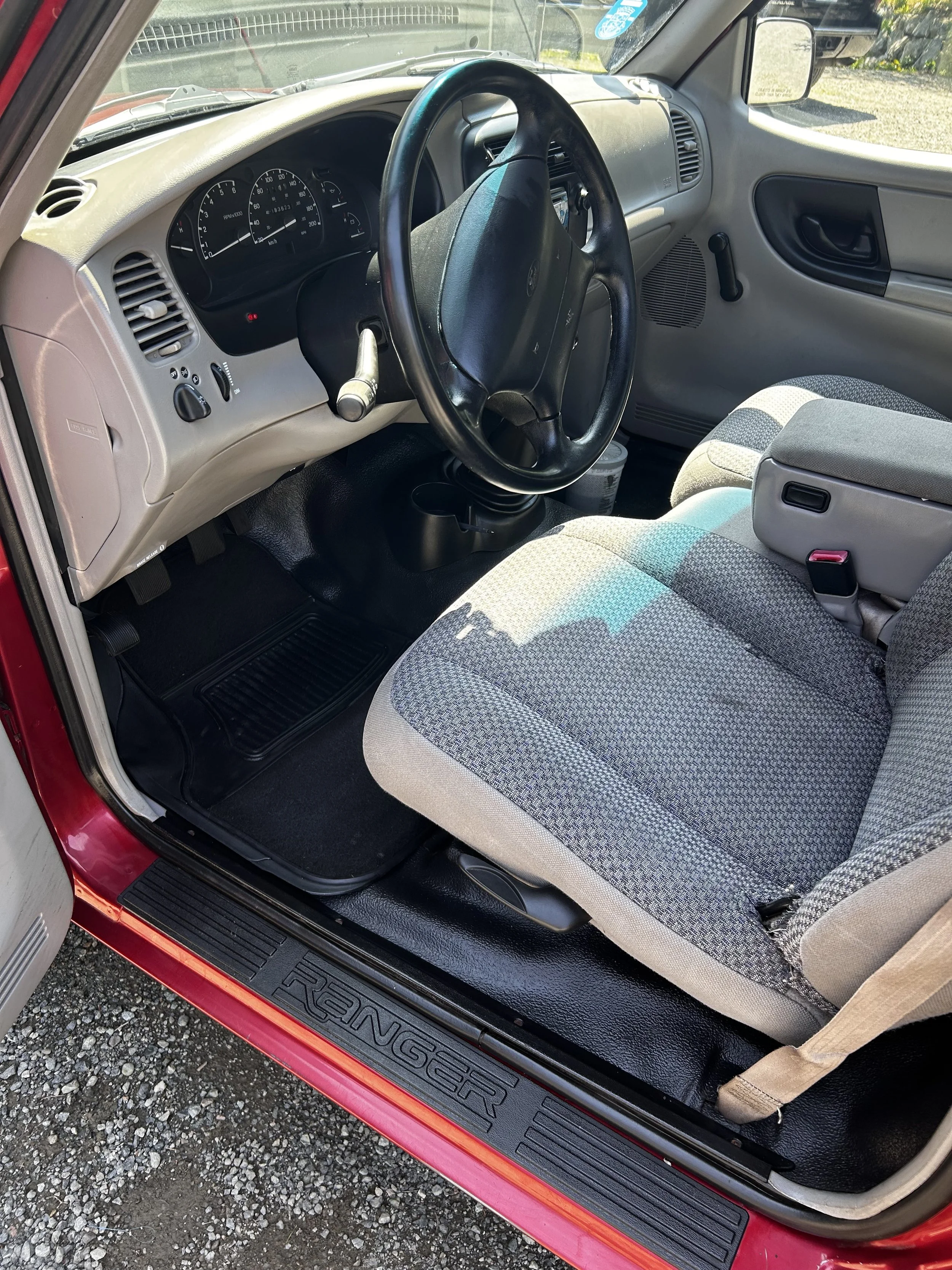 Interior of a red Ford Ranger truck showing the steering wheel, dashboard, driver’s seat, and floor mat with the 'Ranger' logo.