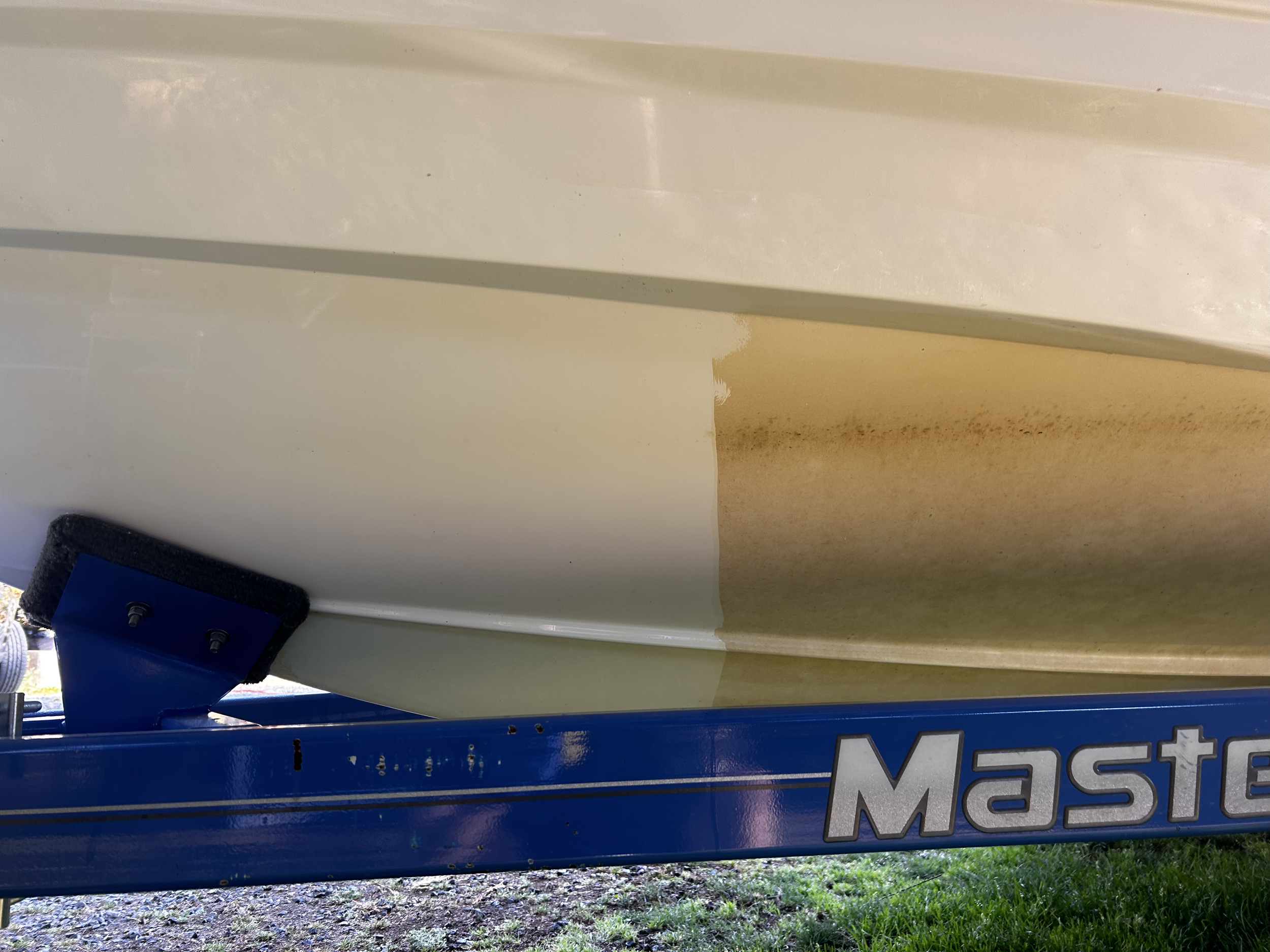 The underside of a boat showing a brown stain or dirt mark on the white hull, supported by a blue boat lift labeled 'Master'.