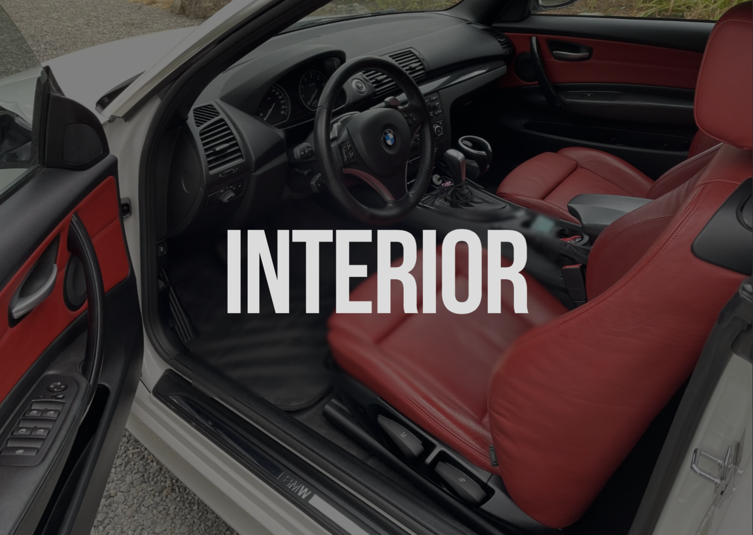 Interior of a car with red leather seats, black dashboard, BMW logo on steering wheel, and open driver's side door showing control buttons.