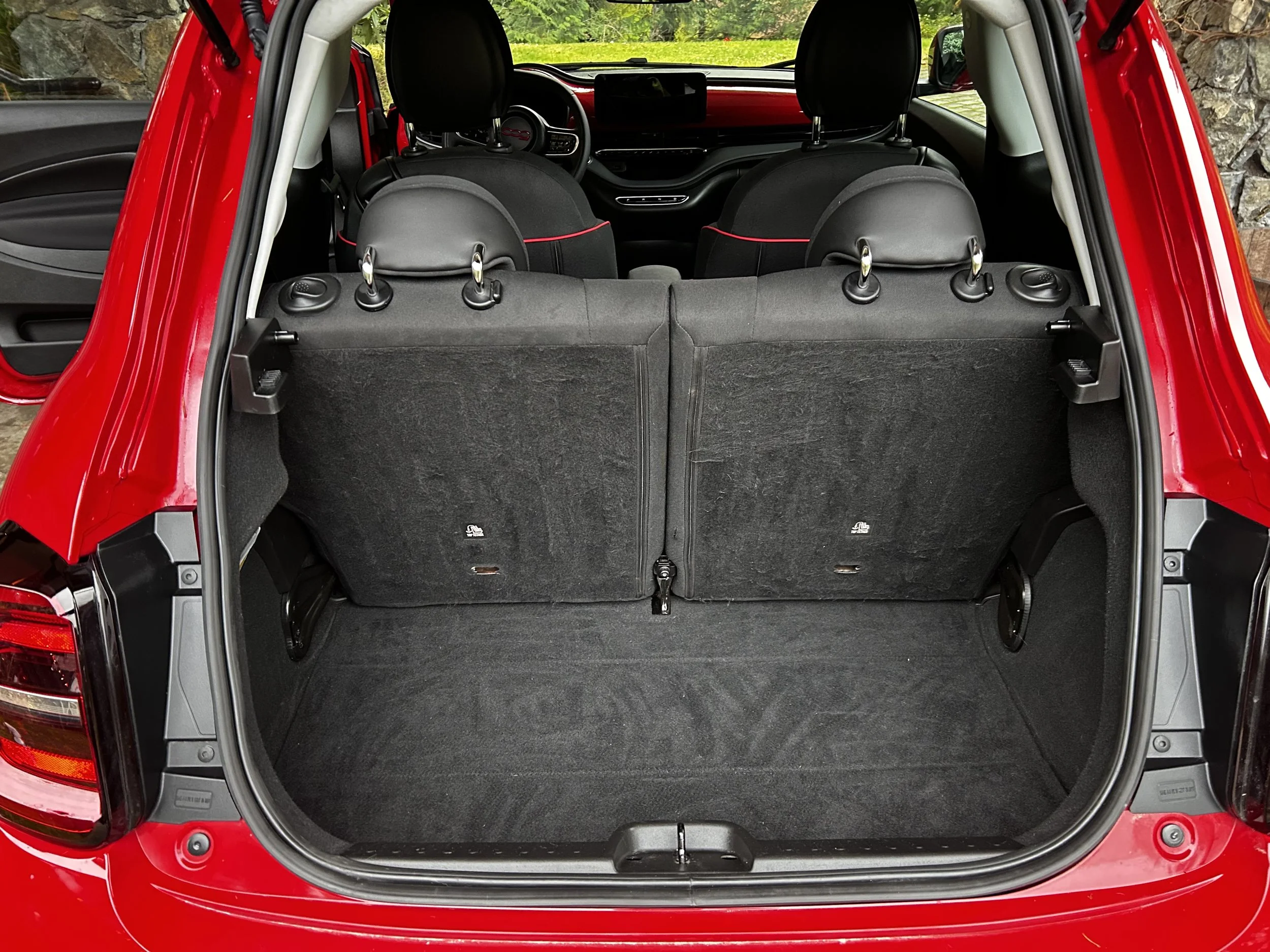 Rear view of a red hatchback car with the trunk open, showing an empty cargo space and the back of the back seats.