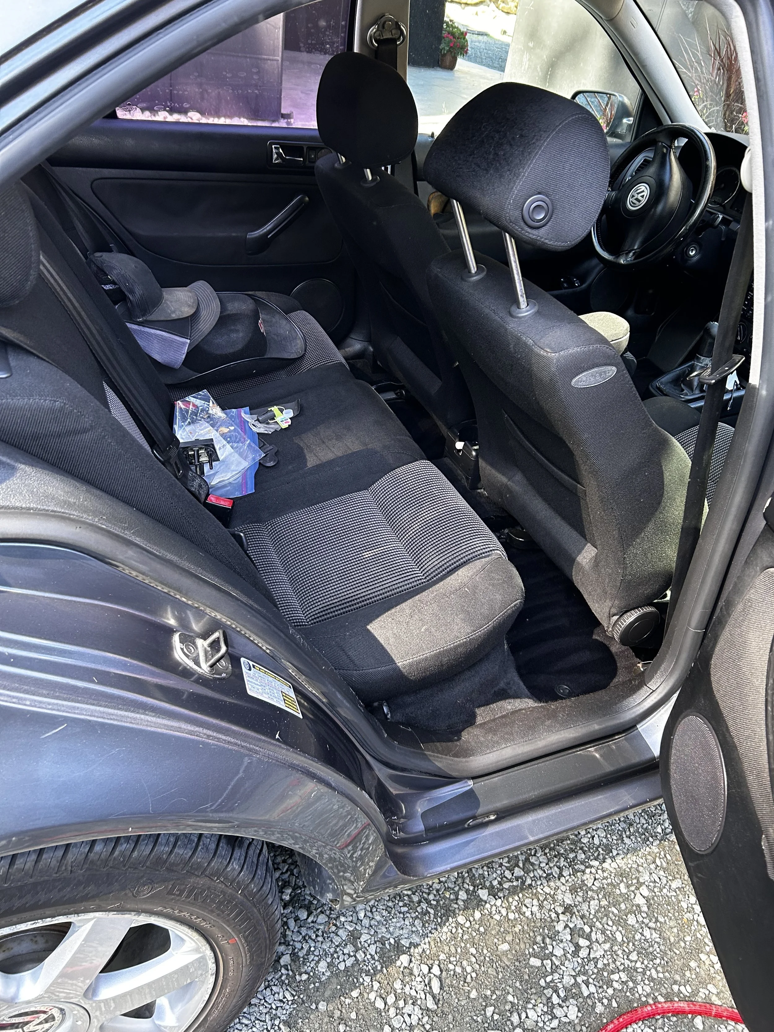 The interior of a car showing the back and front seats, with a child car seat installed in the back and some small items on the seat, and the front dashboard and steering wheel visible.