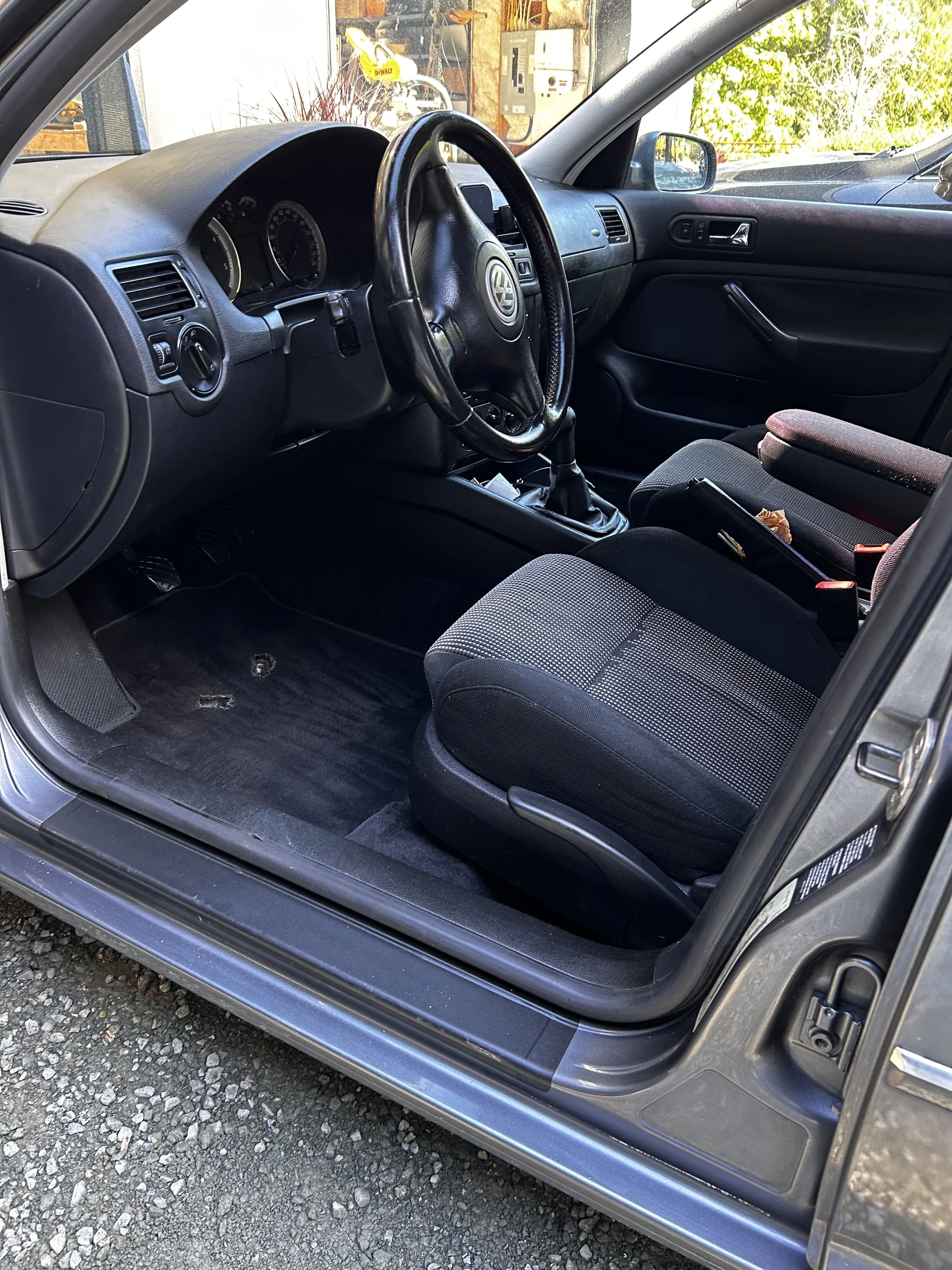 The interior of a gray Volkswagen vehicle showing the driver's seat, steering wheel, dashboard, and front passenger seat. The floor has some dirt and wear marks.