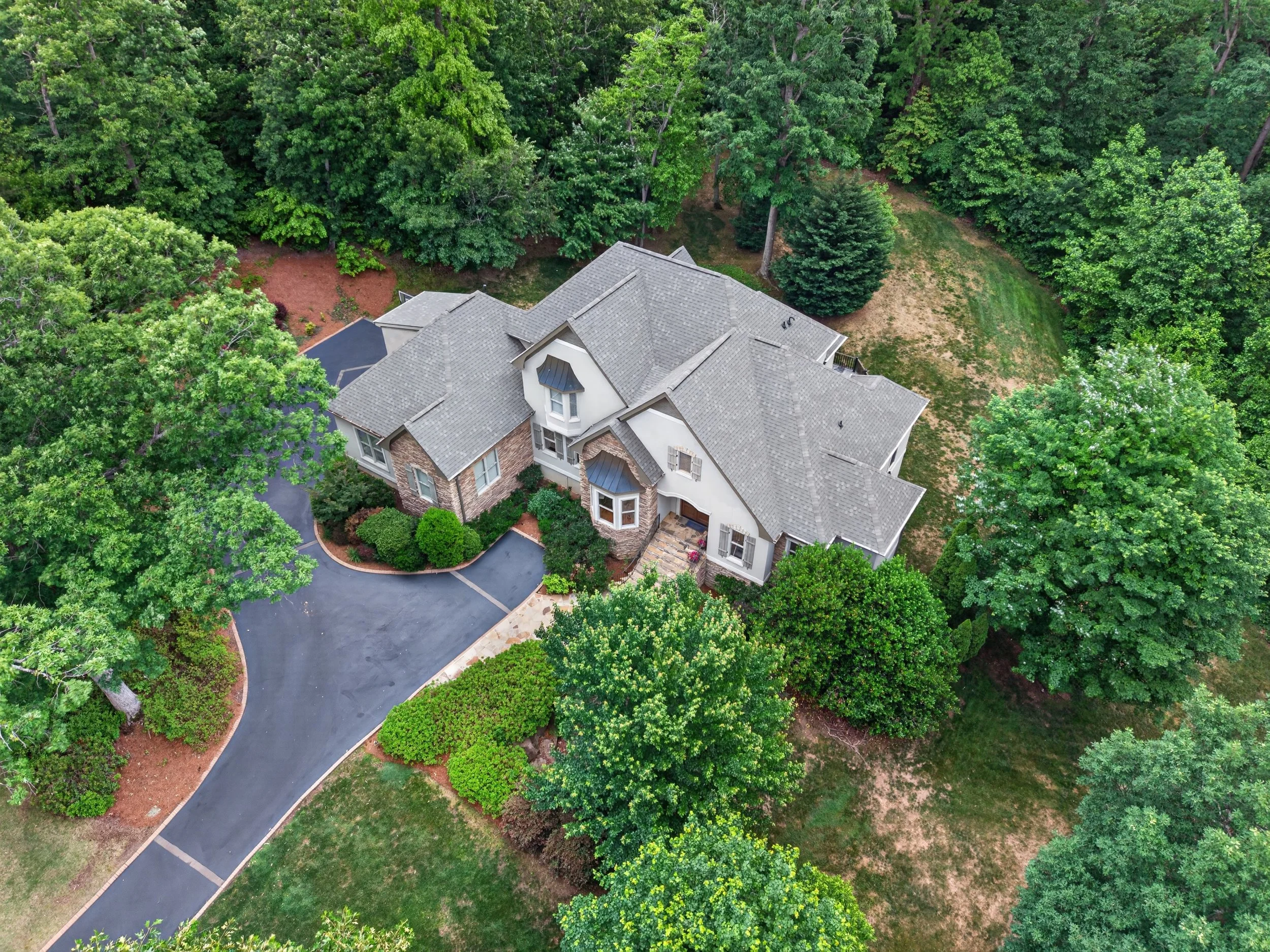 Aerial view of a large house with gray roof, surrounded by trees and green landscape.
