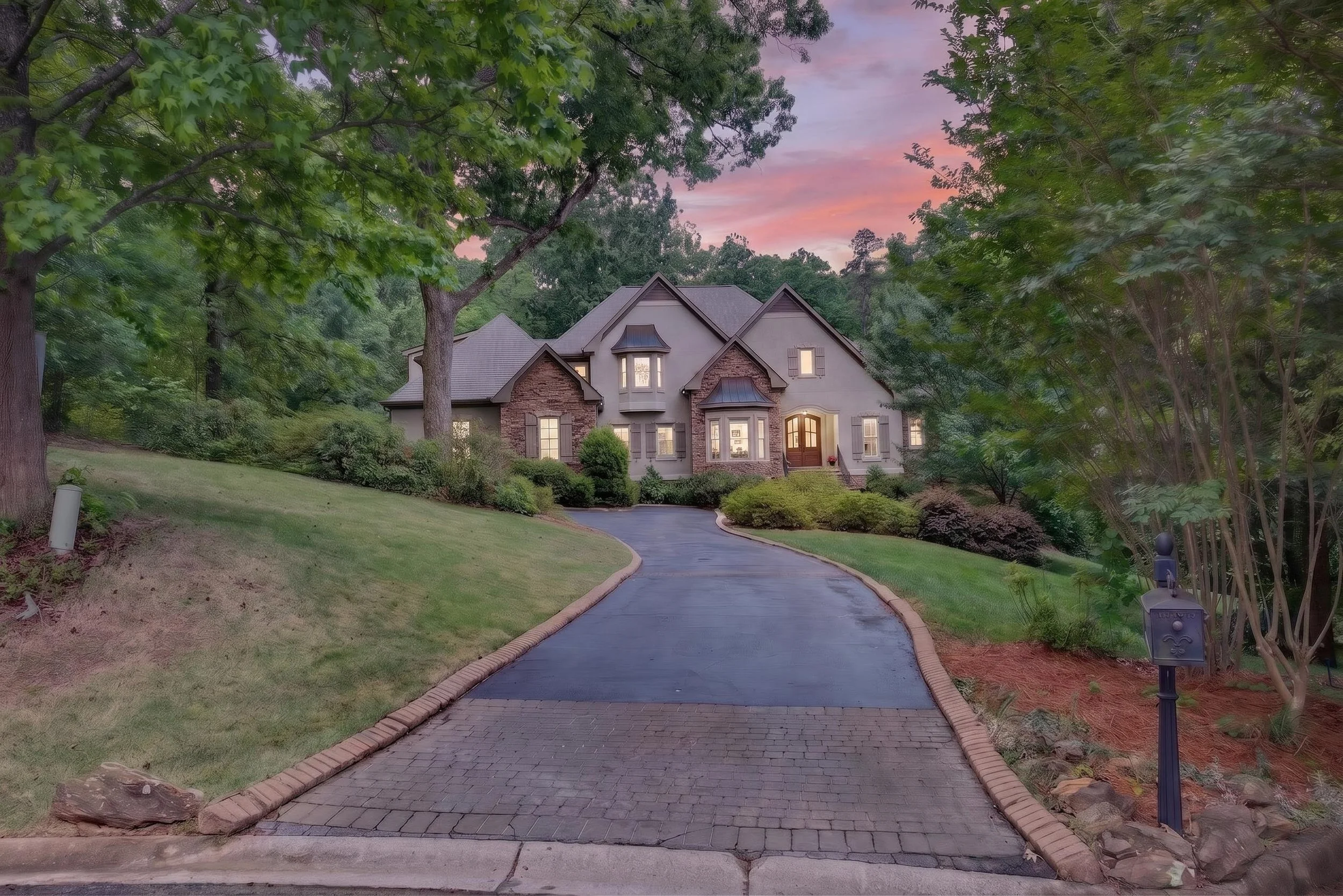 A driveway leading to a large house surrounded by trees at sunset