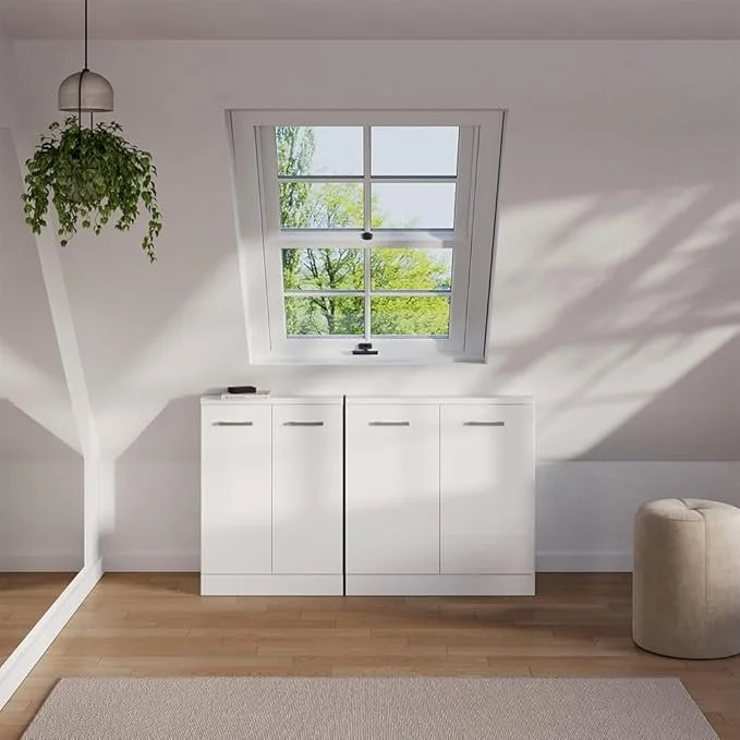 Witte kast onder dakraam in een witte kamer met houten vloer, groene plant en een beige stoel.