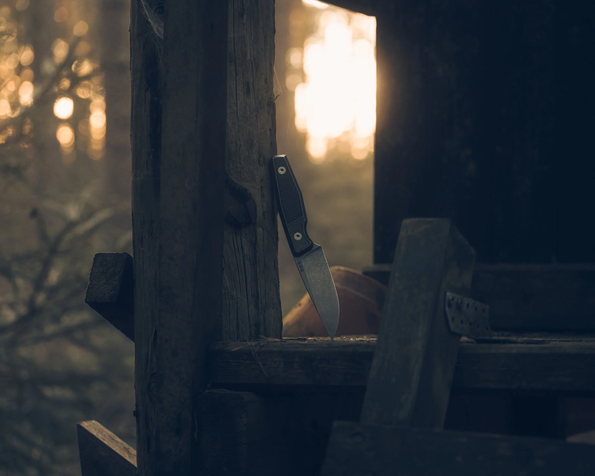Ein Messer steckt in einem Holzbalken in einem idyllischen Sonnenuntergang in einem Wald.