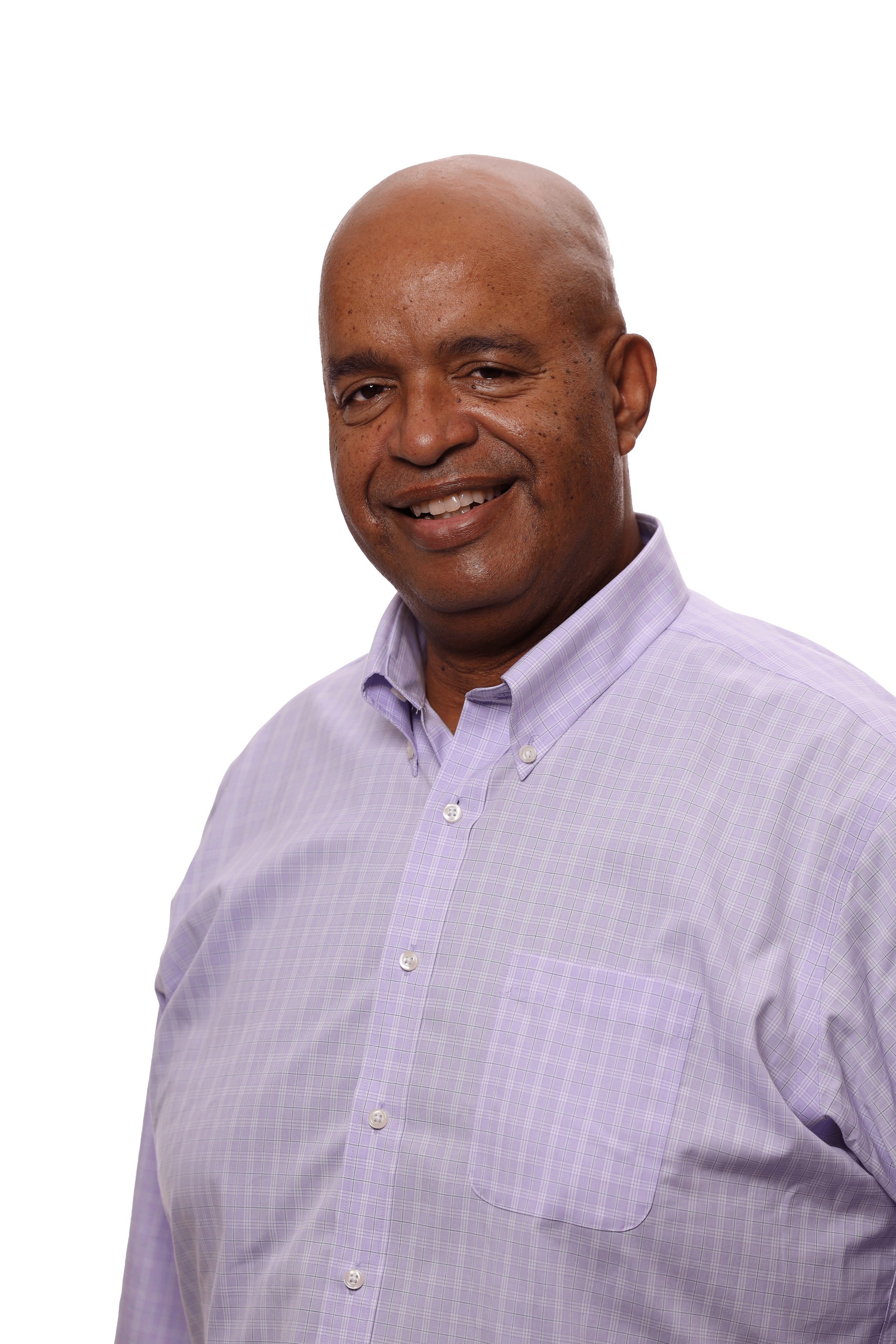 A smiling man with a shaved head, wearing a light purple checkered dress shirt, against a plain white background.